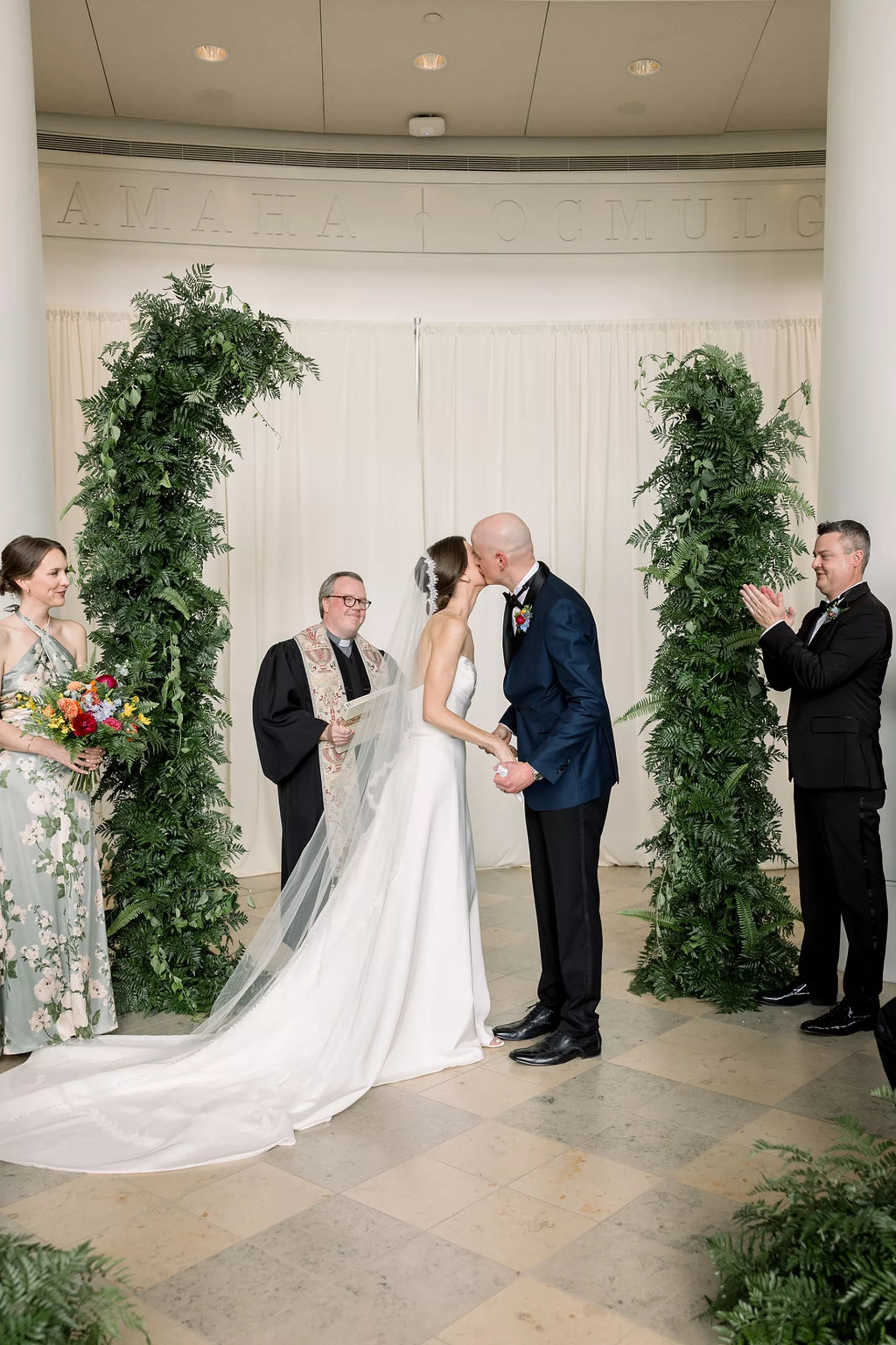 Newlyweds kiss under a fern arch during their jurassic park wedding ceremony
