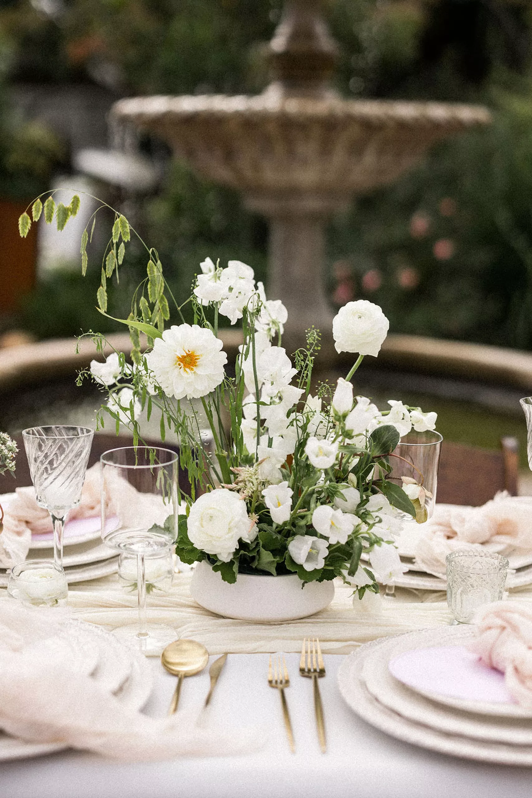 Details of an outdoor wedding reception table set up with pink linen and gold silverware next to a fountain at lillian gardens wedding venue