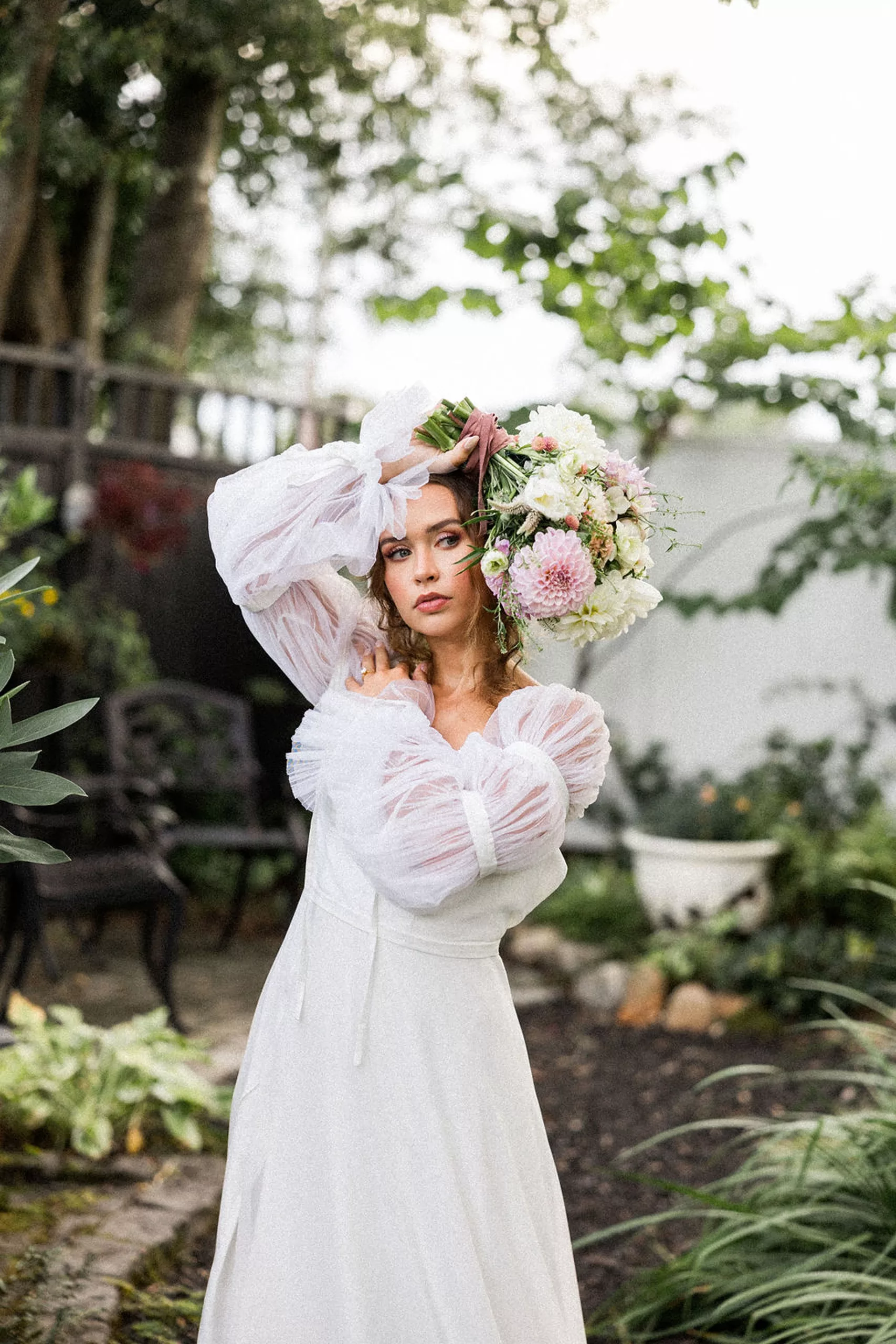 A bride holds her colorful bouquet over her head in a white dress while standing in a garden path