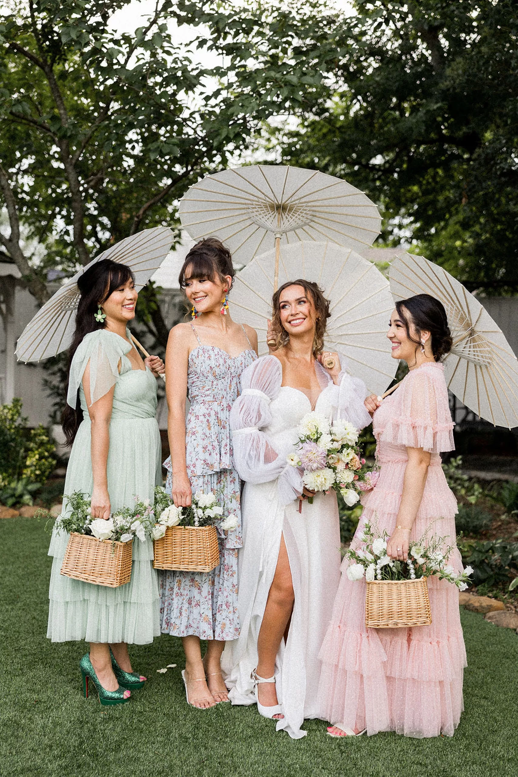 A bride stands in a garden holding umbrellas with her three bridesmaids