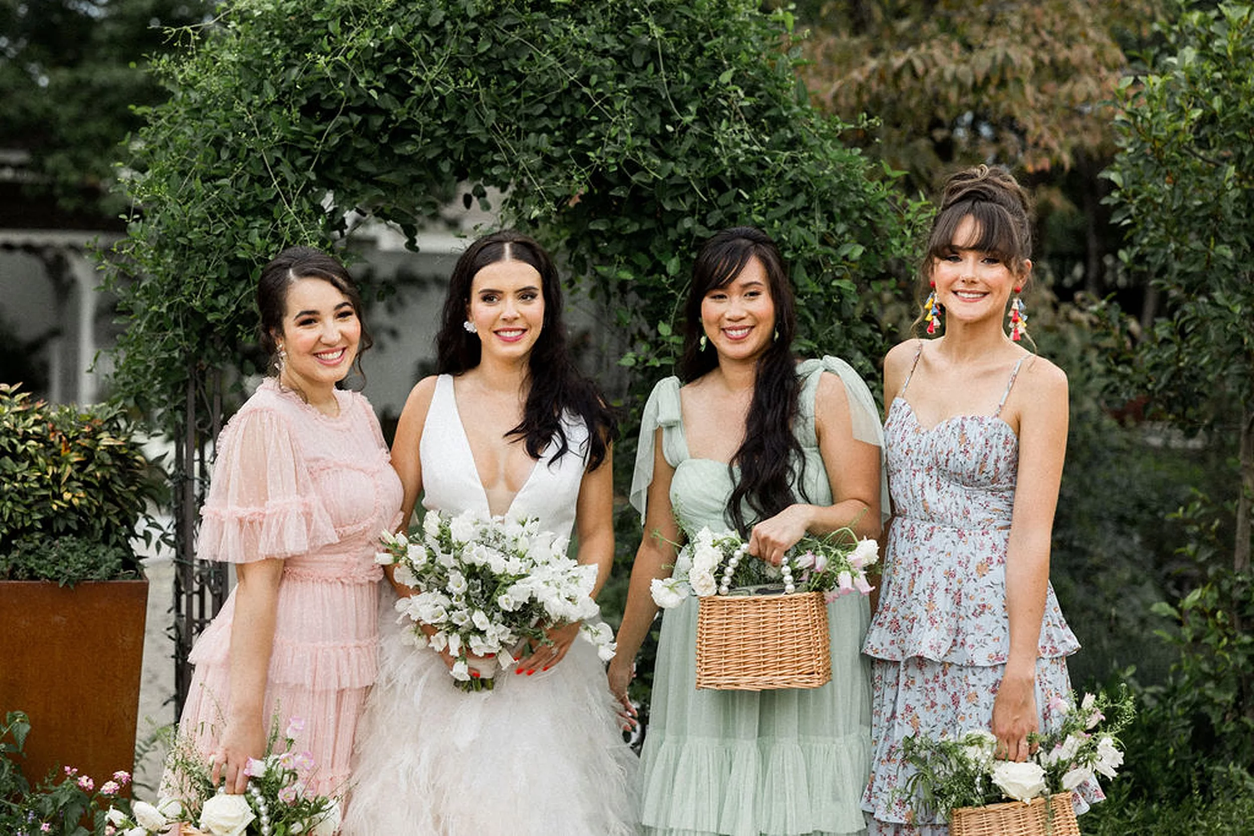 A bride stands with her bridesmaids holding wicker and pearl bouquet baskets