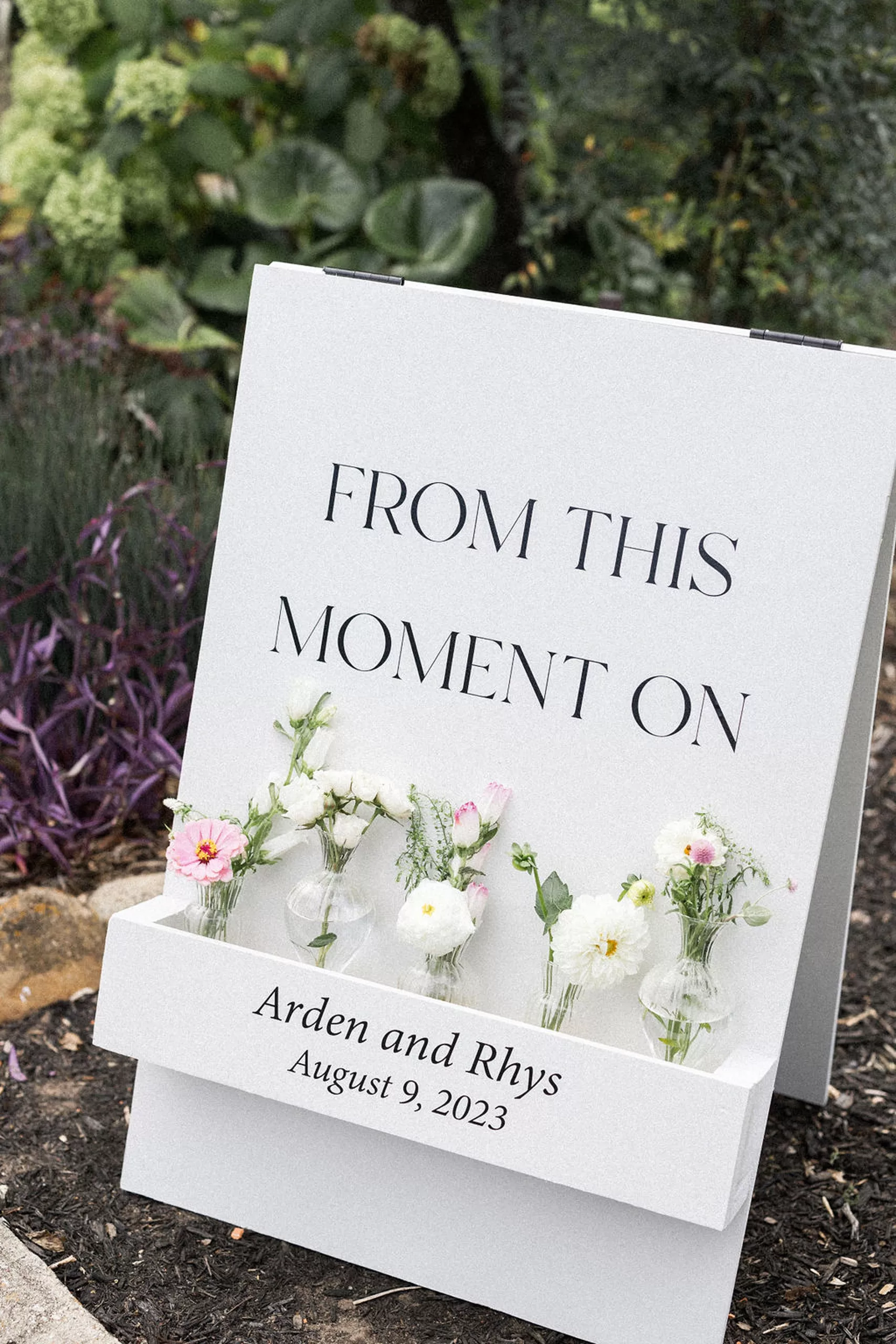 Details of a wedding sign set up in a garden with florals