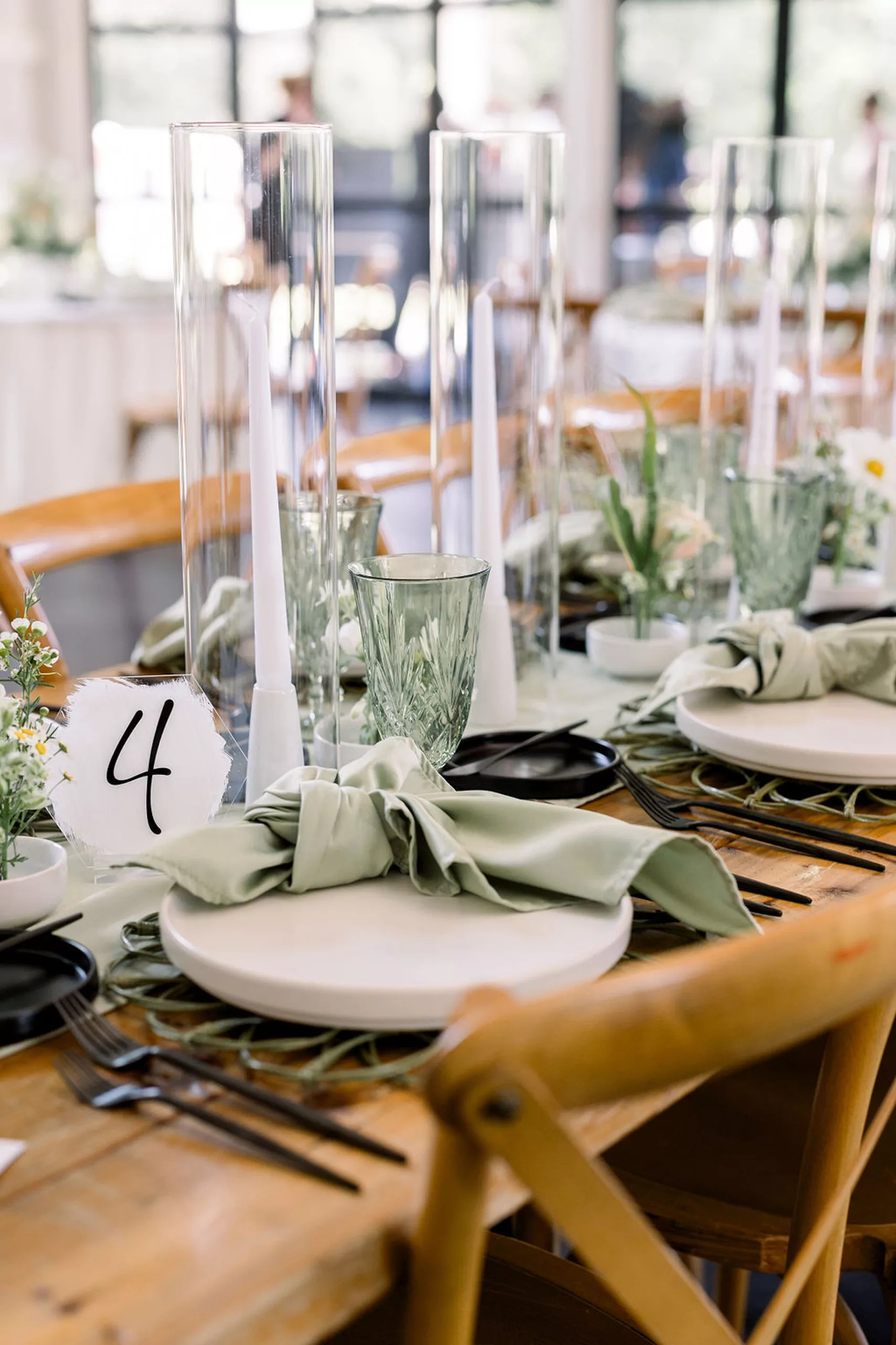 Details of a table setting on wood with wood chairs and green glasses and napkins