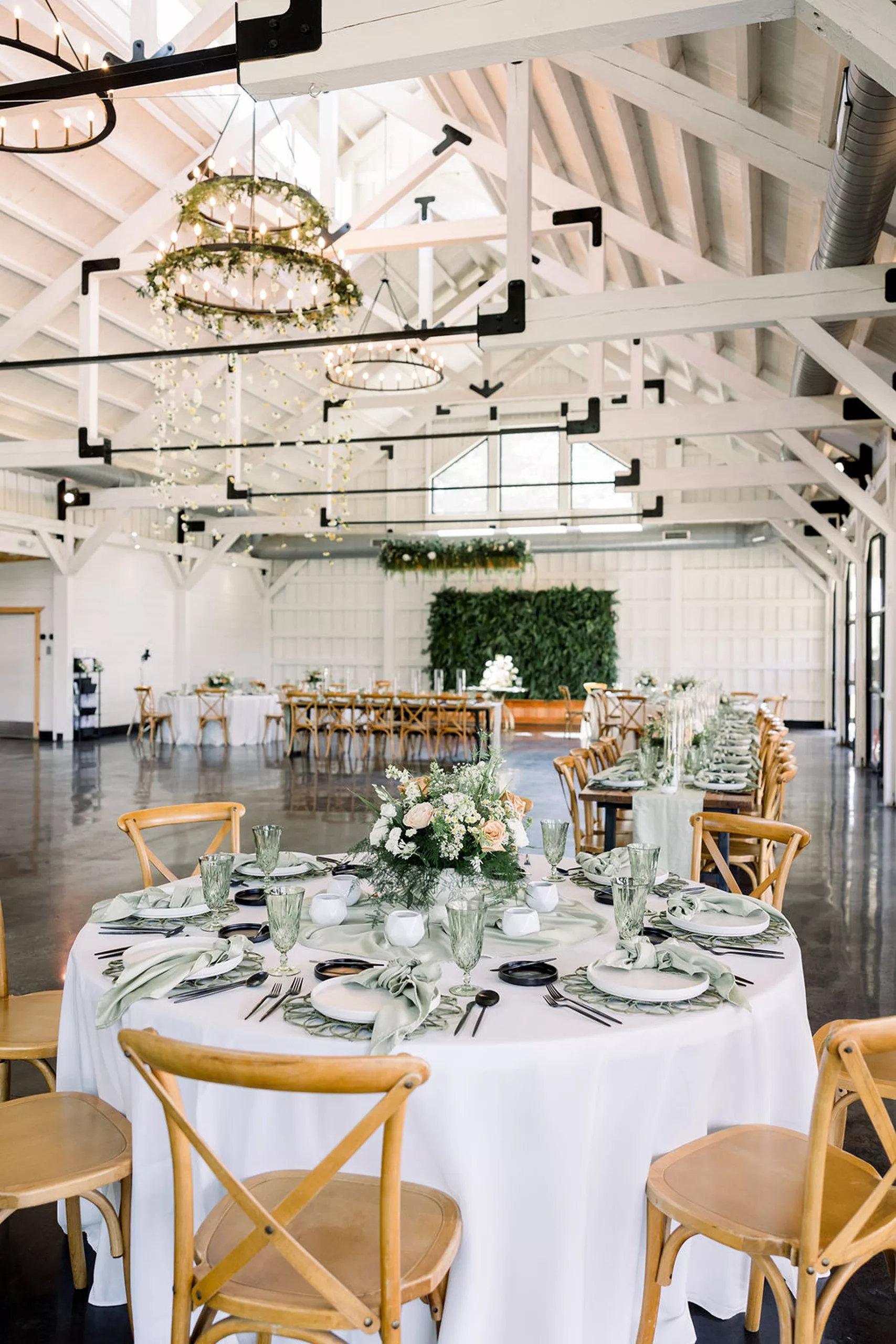 Details of a wedding reception venue set up with white exposed beams, chandeliers and white linens