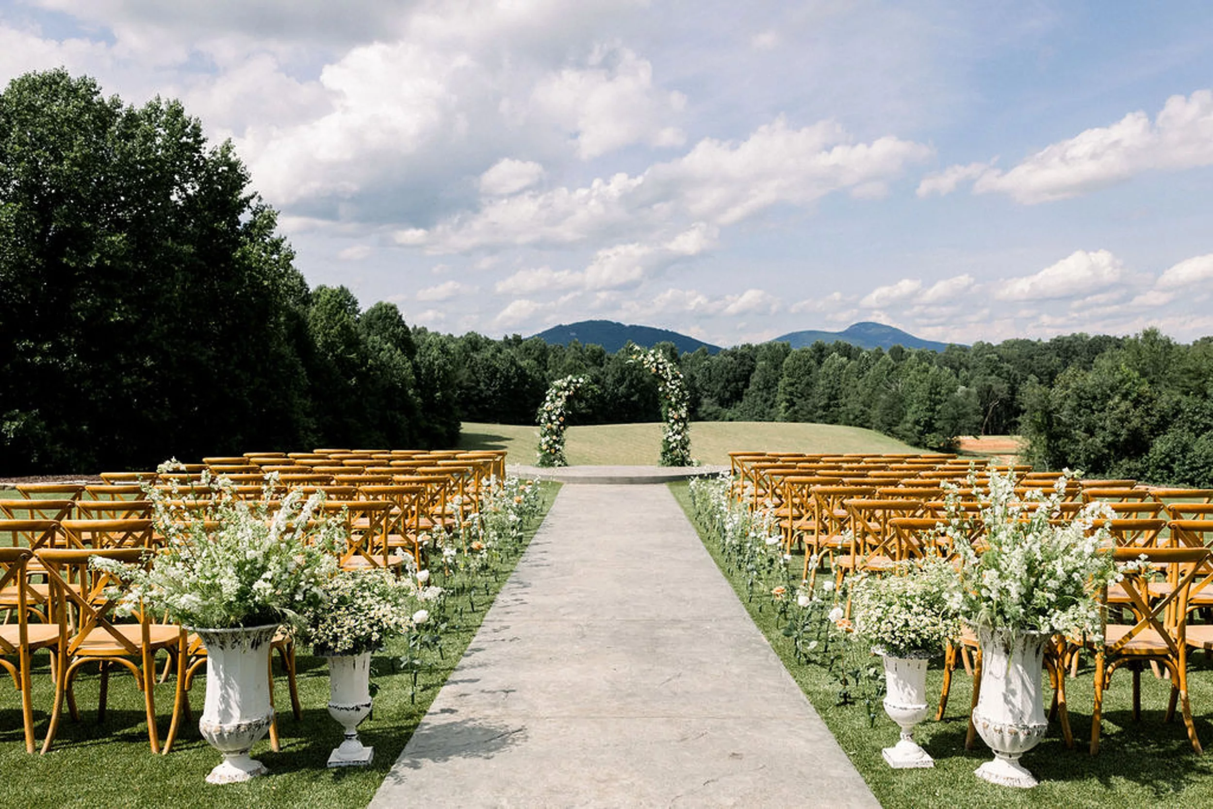 Details of a wedding ceremony set up in a lawn with a floral arch with wooden chairs