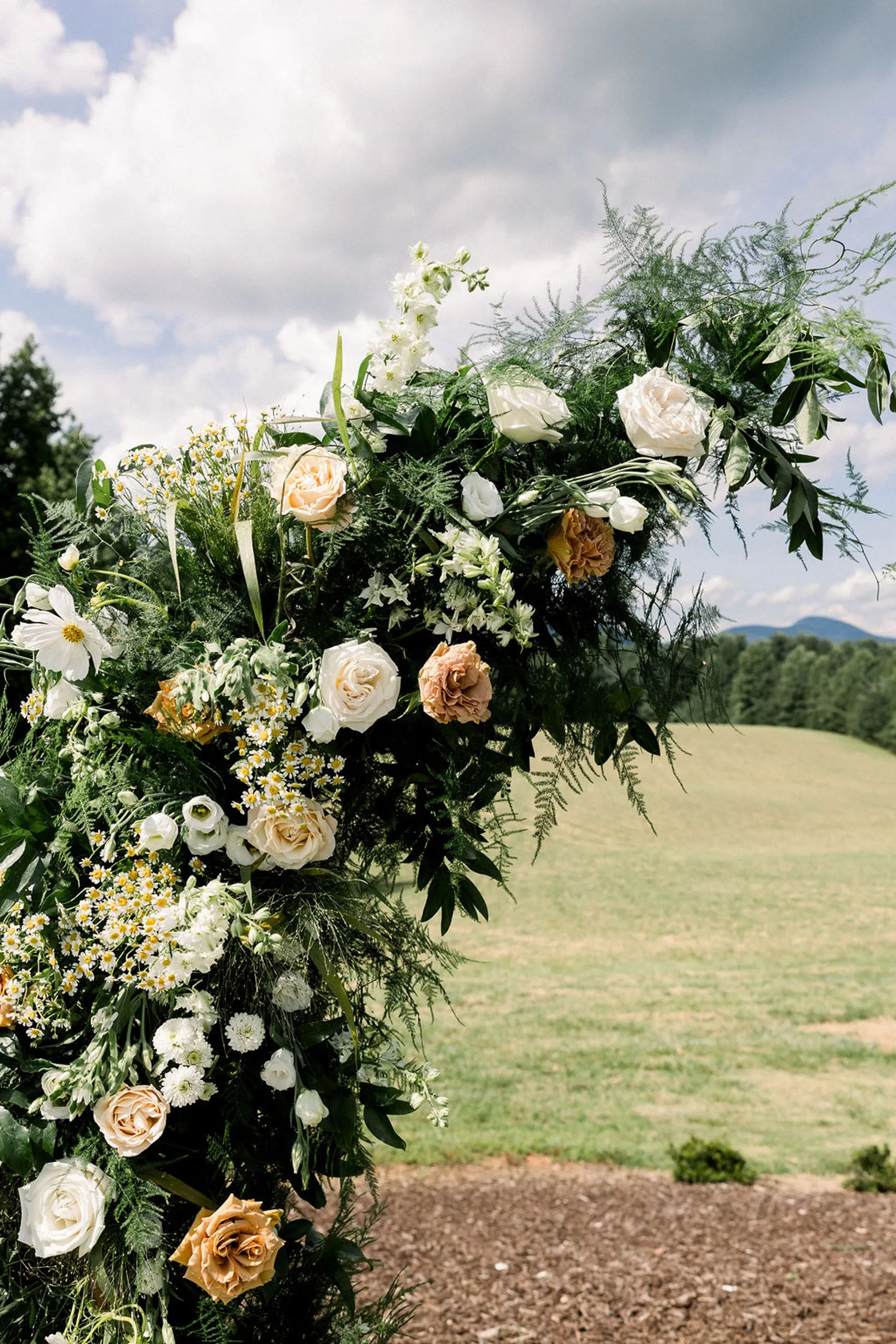 Details of a wedding arch with white and orange roses in an open field at a meadows at mossy creek wedding