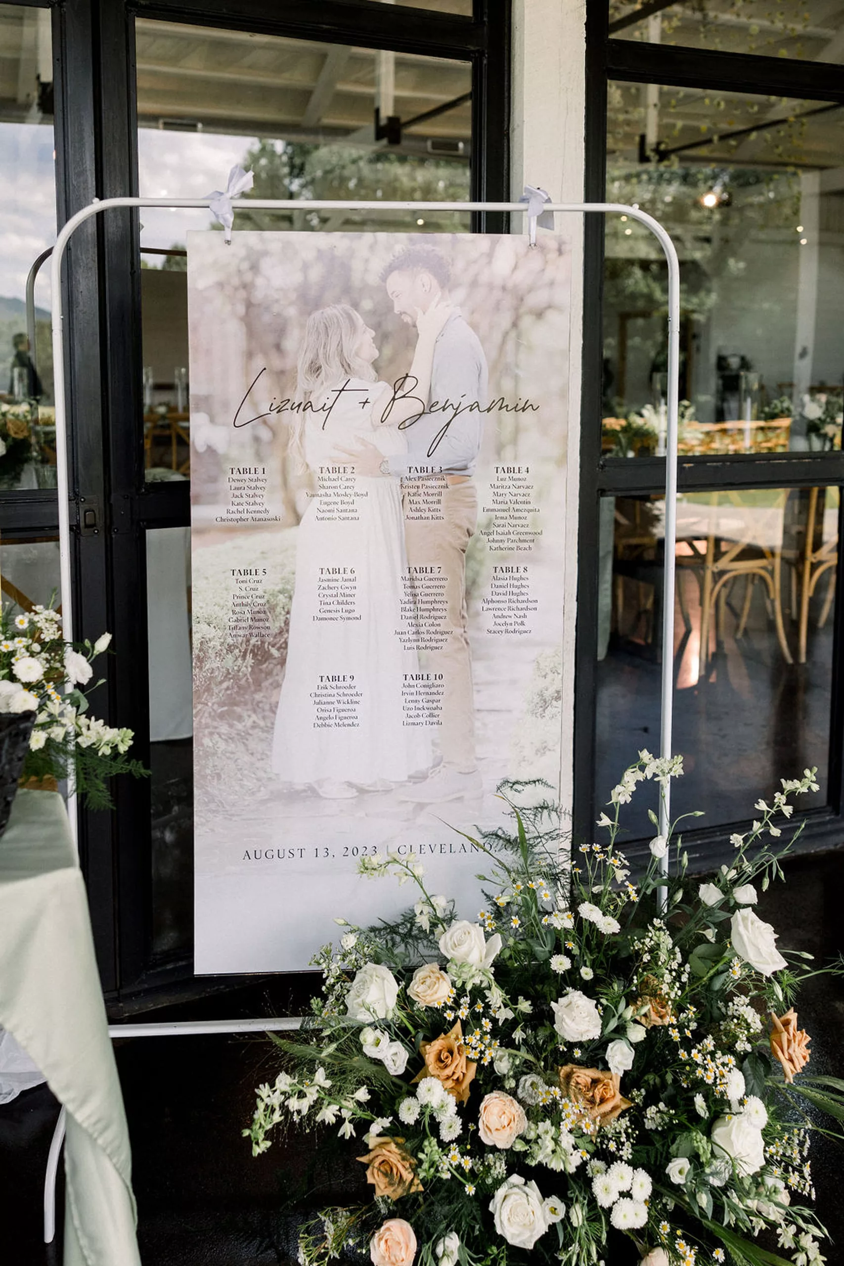 Details of a wedding reception table assignment hanging behind a large white and orange floral