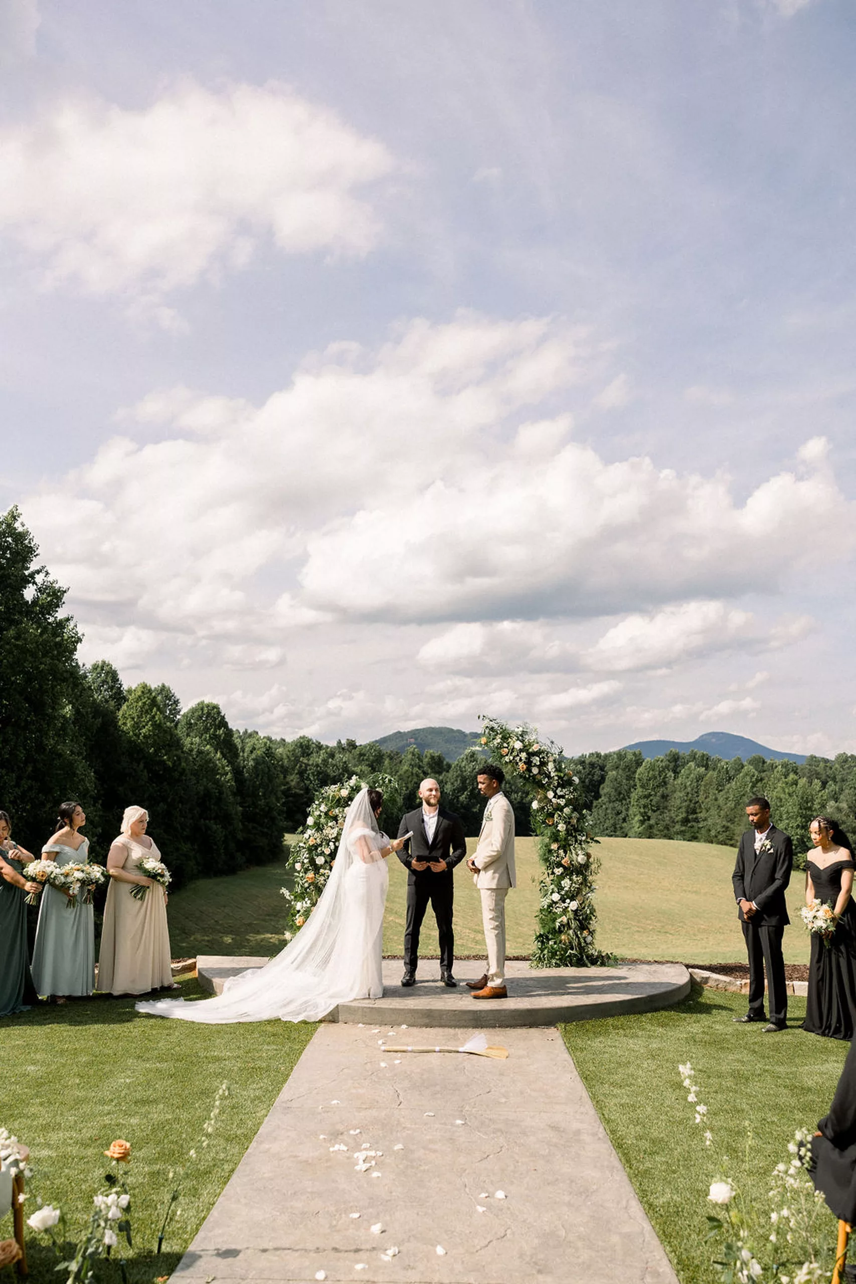 NEwlyweds stand at the altar of their outdoor ceremony in a large grass field with their officiant and bridal parties at a meadows at mossy creek