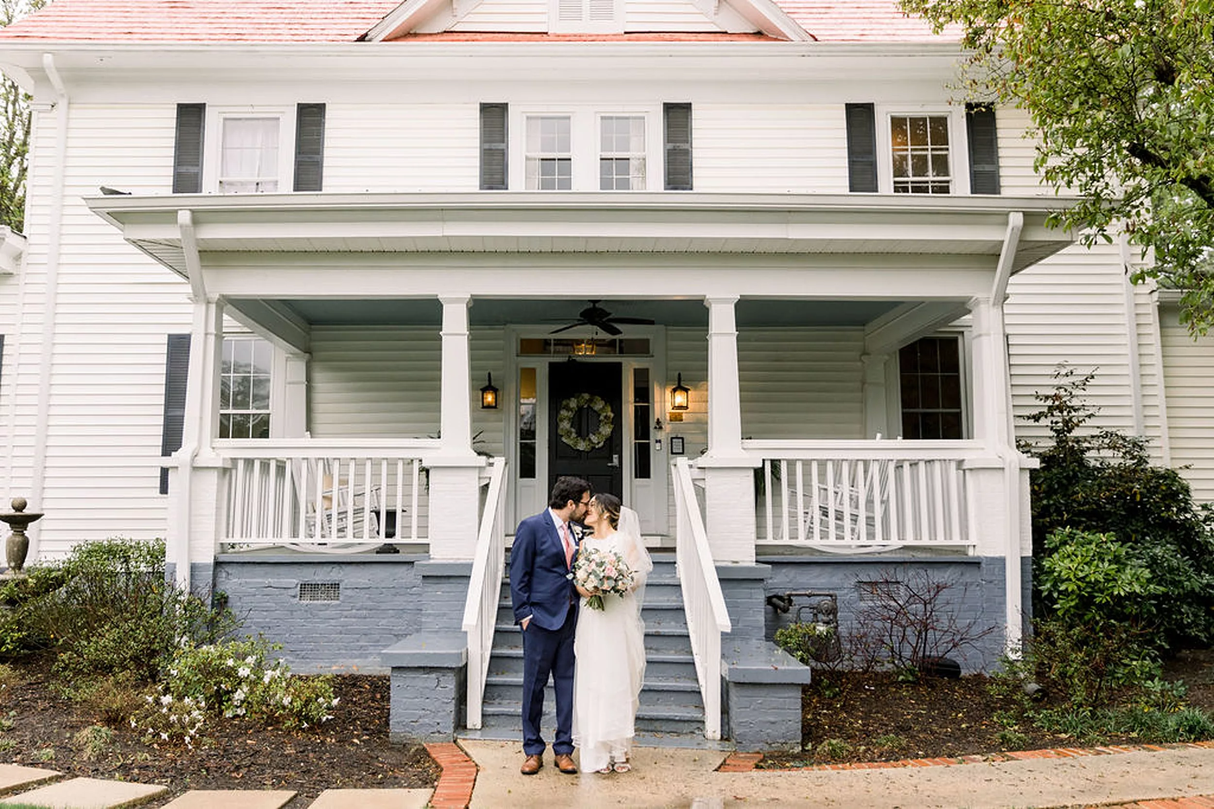 Newlyweds kiss in front of a porch at the payne-corley house wedding venue