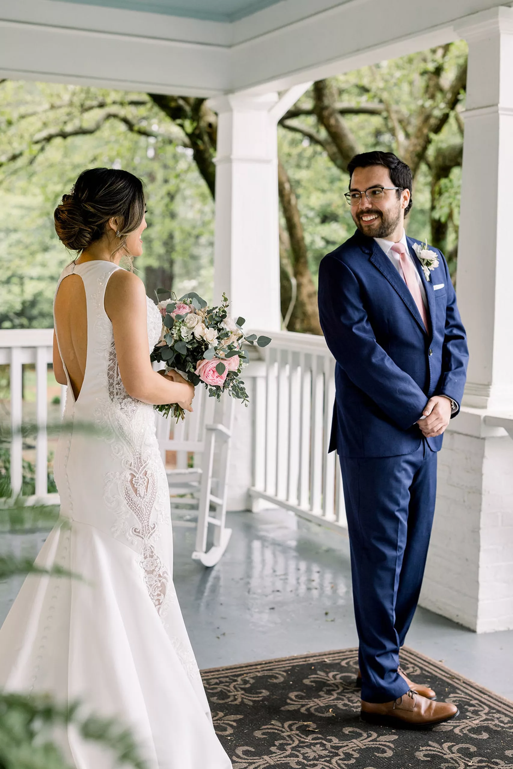 A groom turns around on a porch to see his bride for the first time in her dress during a first look