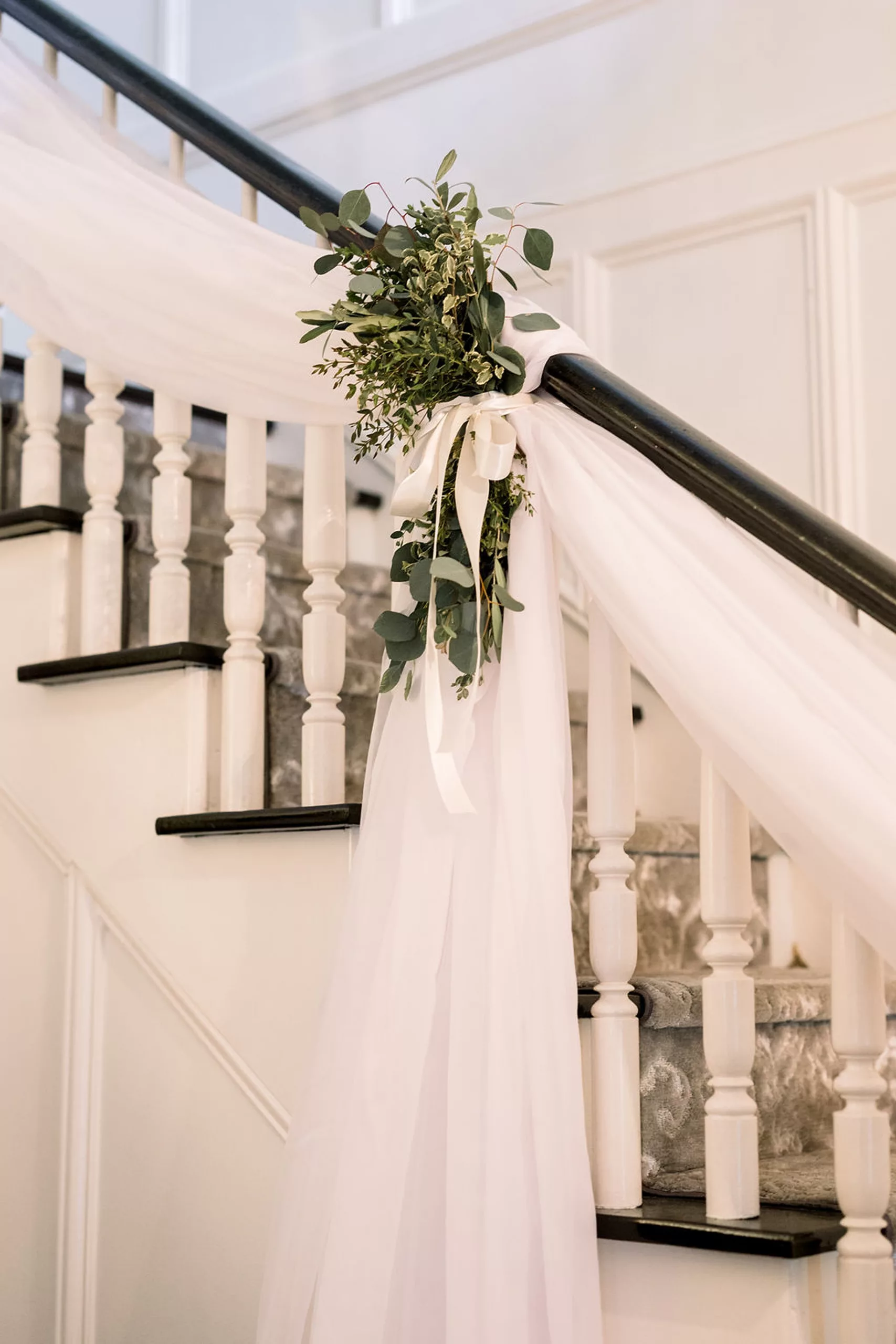 Details of white linens and florals hanging from a handrail on stairs at a payne-corley house wedding