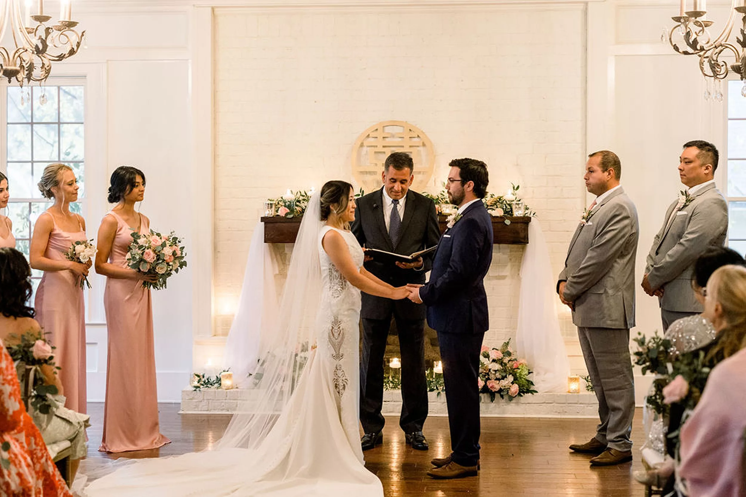 Newlyweds hold hands in front of a fireplace and their officiant during their payne-corley house wedding ceremony