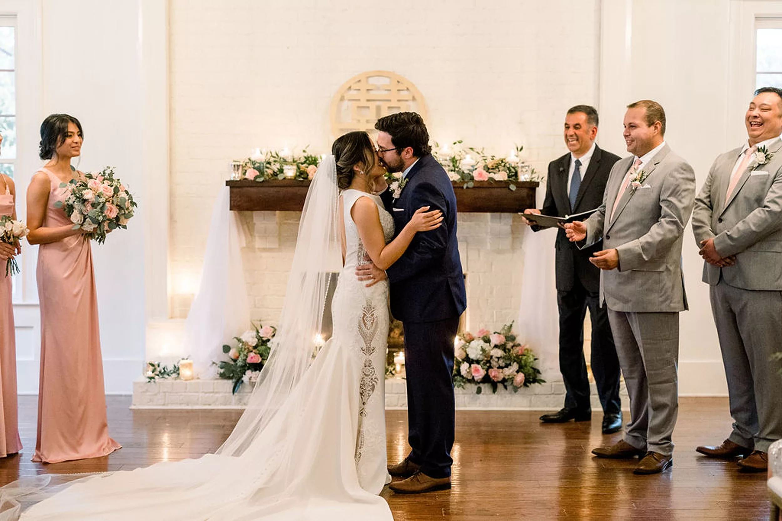 Newlyweds kiss at the altar with their bridal party and officiant smiling around them at a payne-corley house wedding