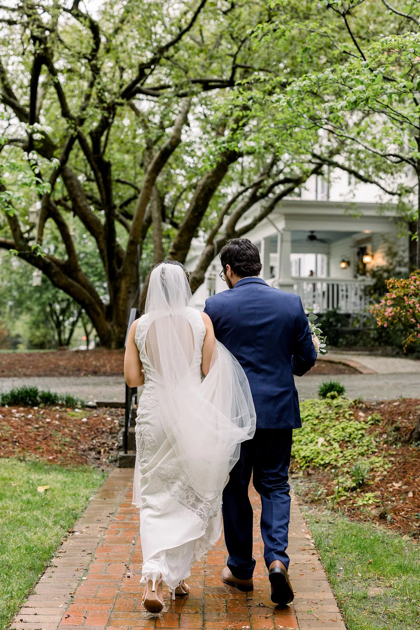 Newlyweds walk through some rain in a garden holding hands and the train back to the payne-corley house wedding venue