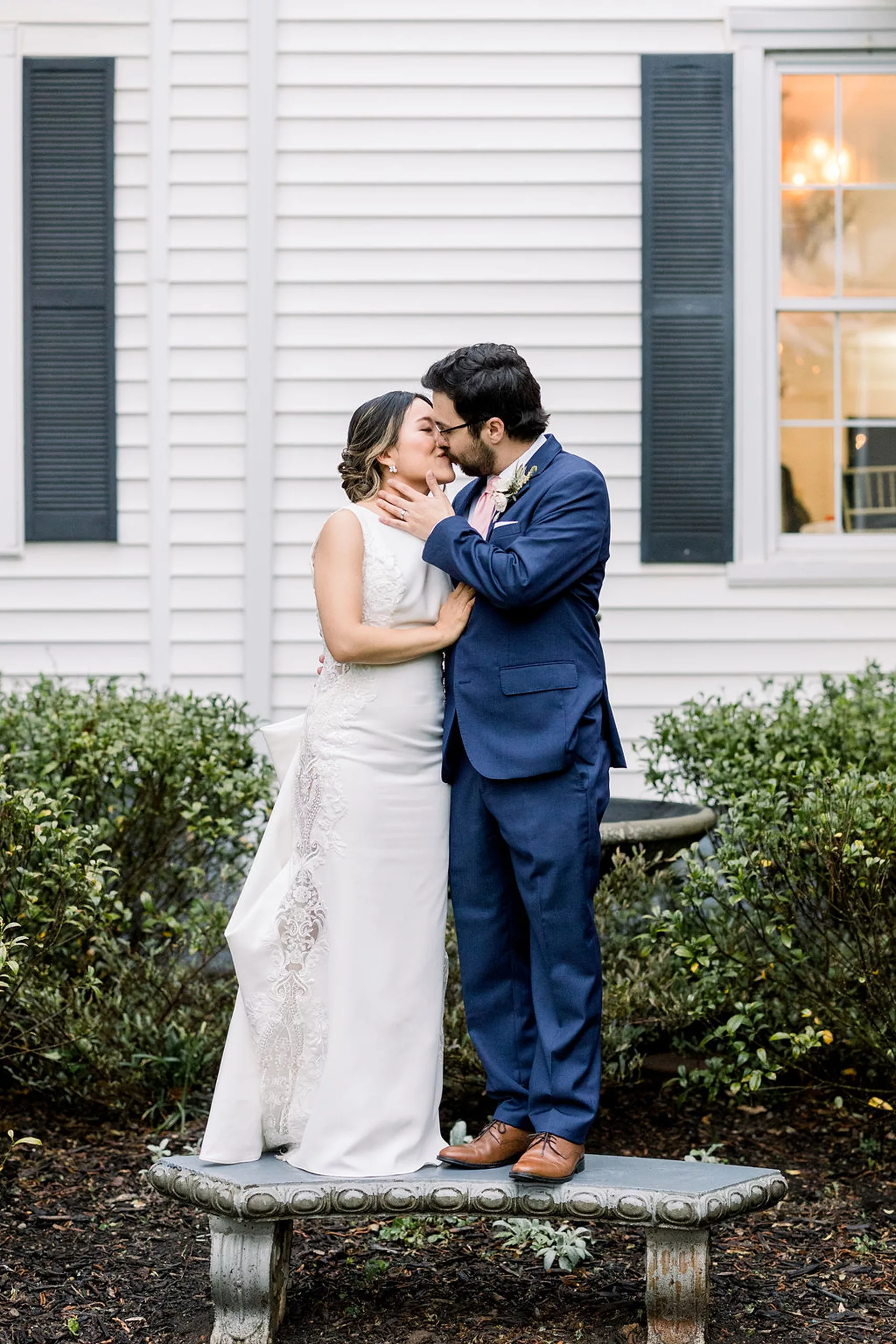 Newlyweds stand on a garden bench kissing outside the payne-corley house wedding venue