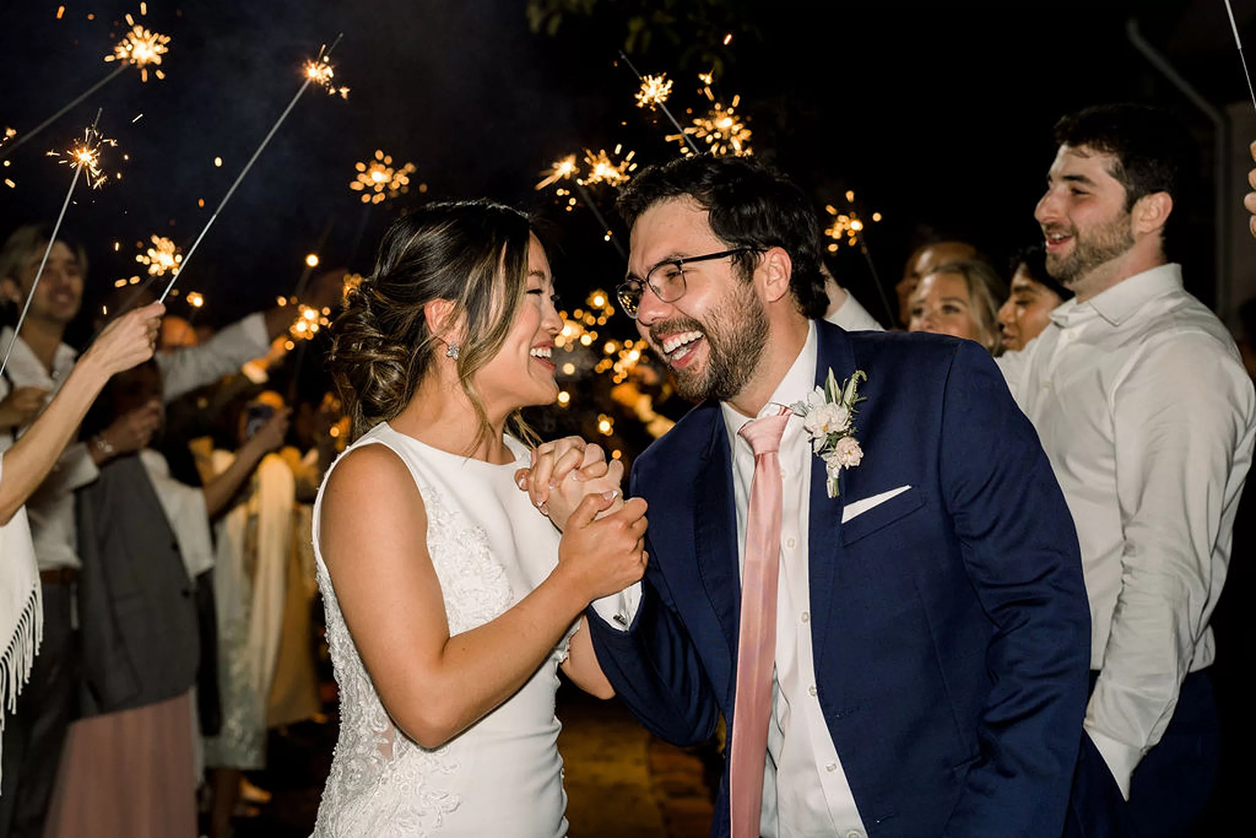 Newlyweds hold hands and laugh as they walk under a shower of sparklers being held up by their payne-corley house wedding guests