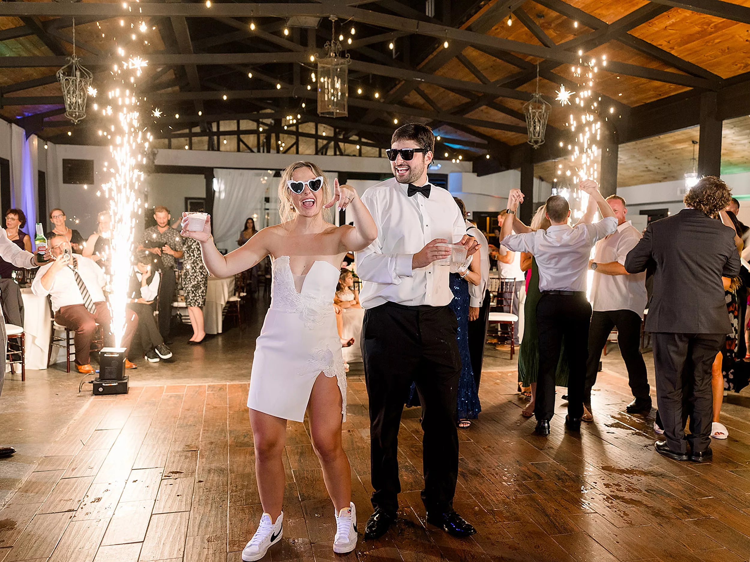 Newlyweds party and dance on the dance floor with sparklers going off around them while wearing sunglasses at a White Oaks Vineyard wedding