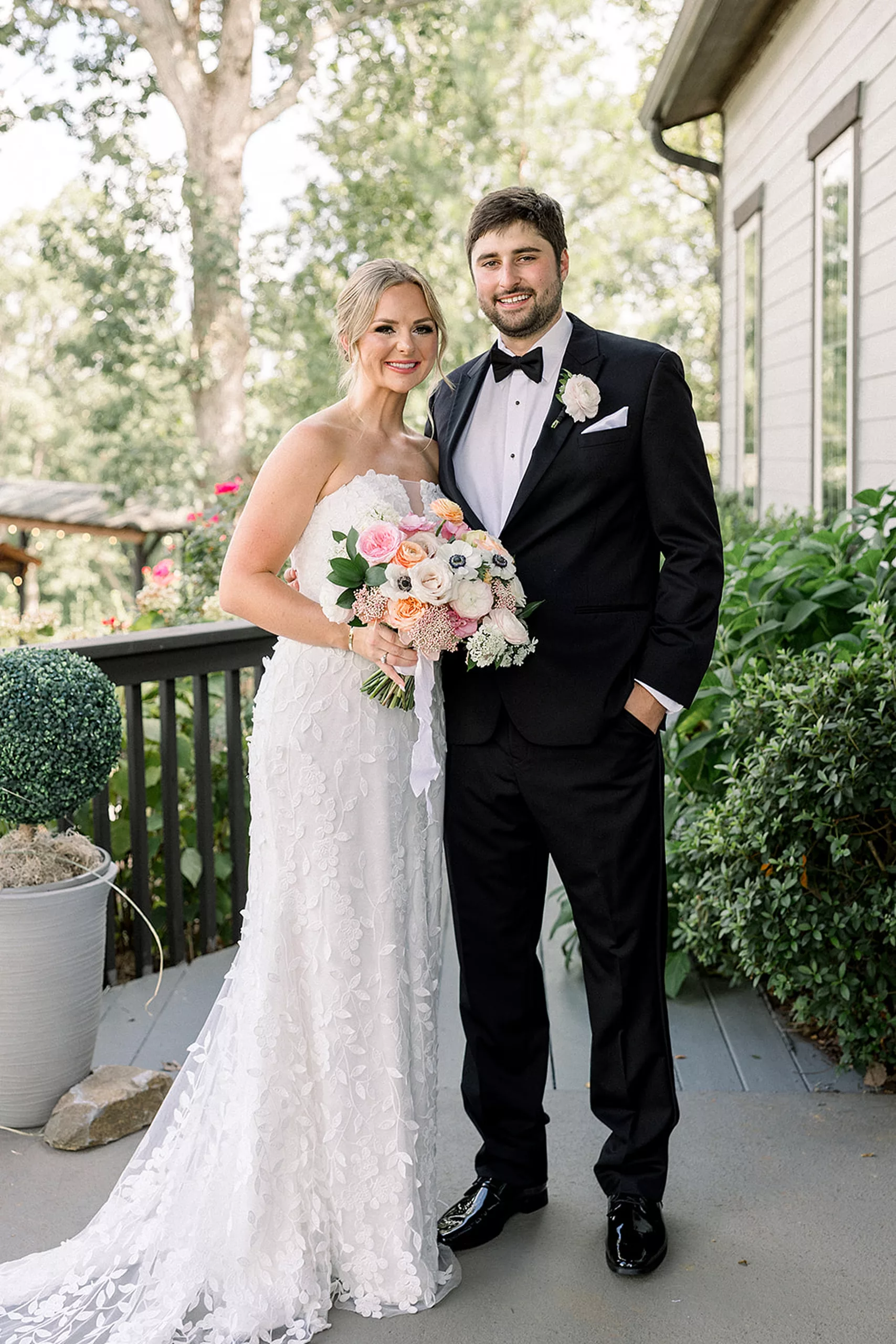 Newlyweds wrap their arms around each other while standing on a porch