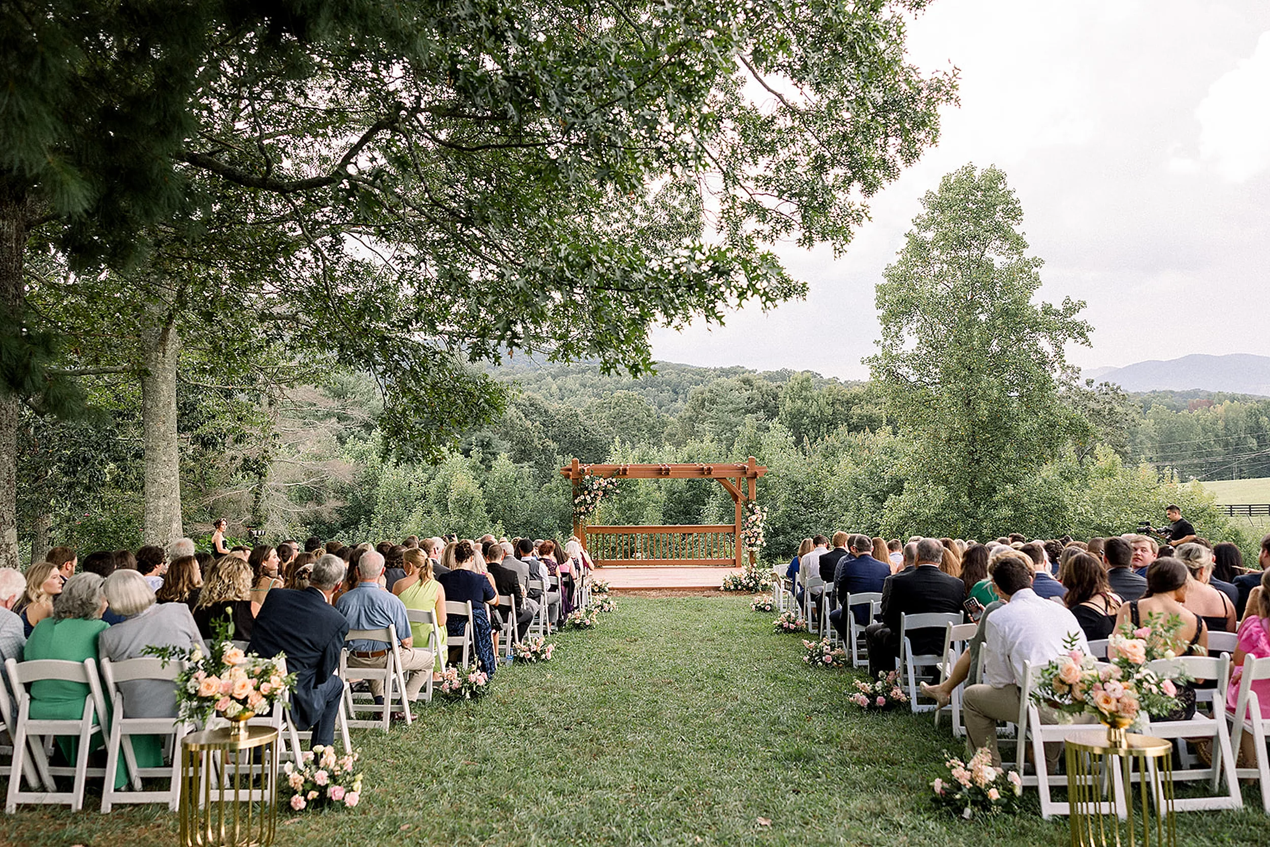 Guests sit in white chairs waiting for an outdoor White Oaks Vineyard wedding on a hill