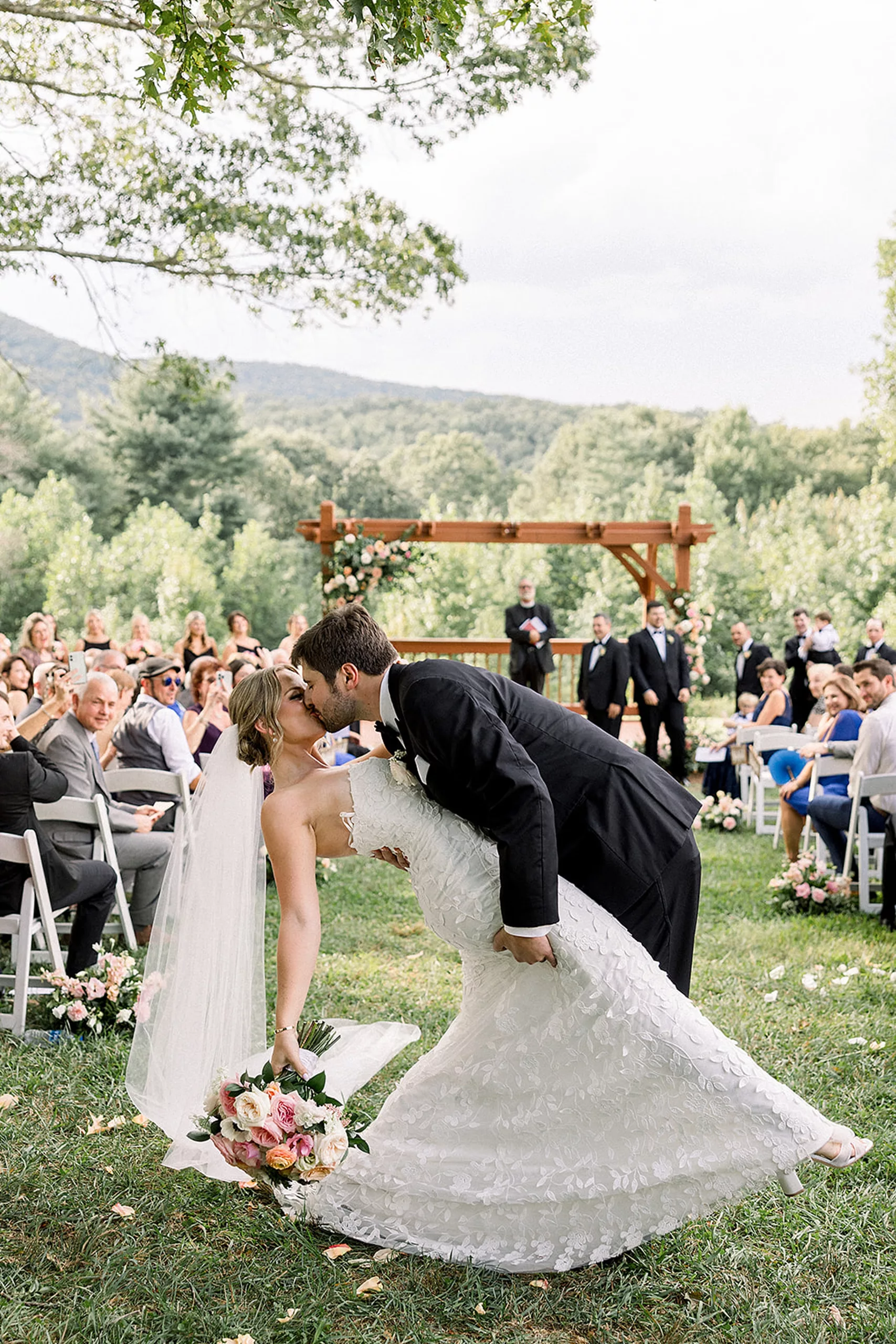 Newlyweds kiss at the end of the aisle following their ceremony with guests looking on from their chairs at an outdoor White Oaks Vineyard wedding ceremony
