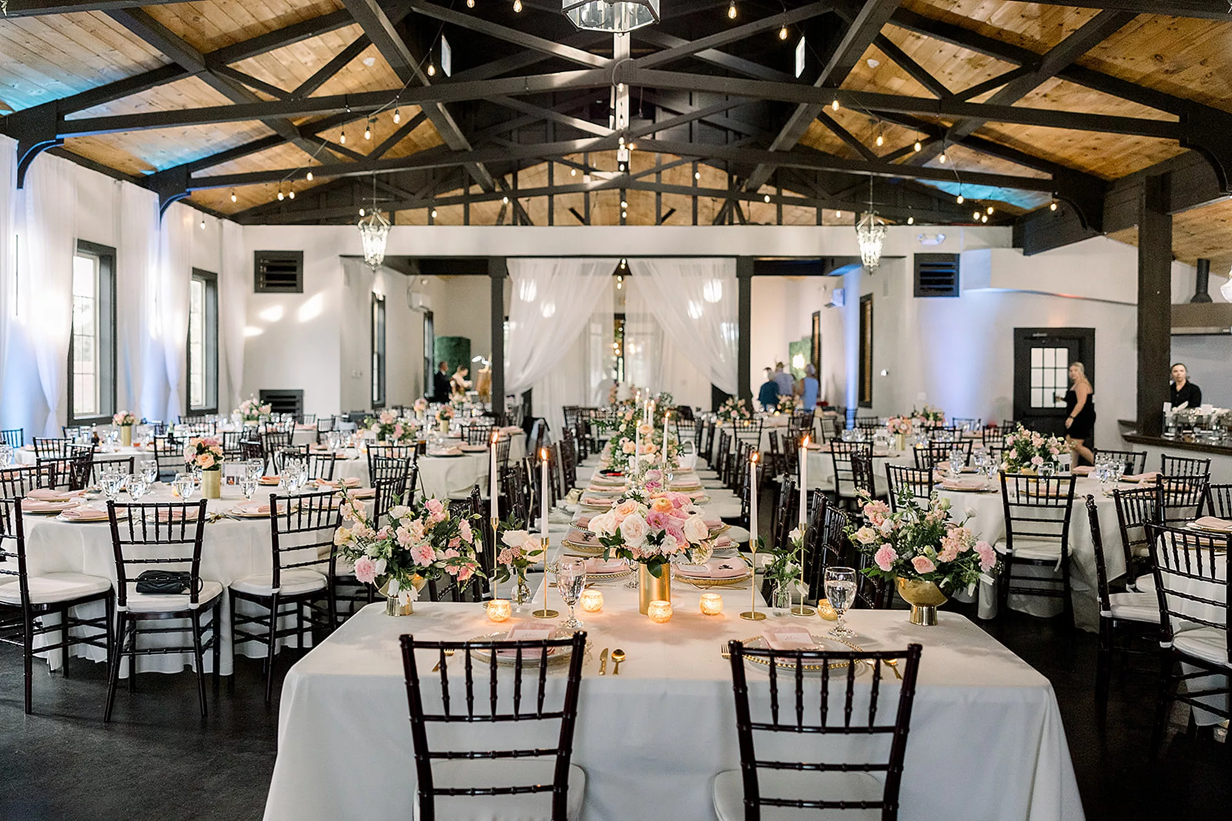 Details of a wedding reception set up in the White Oaks Vineyard ballroom with white linens, pink napkins and black chairs with exposed ceilings