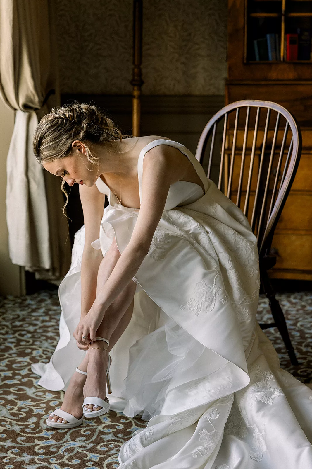 A bride sits in her getting ready room fixing her shoes
