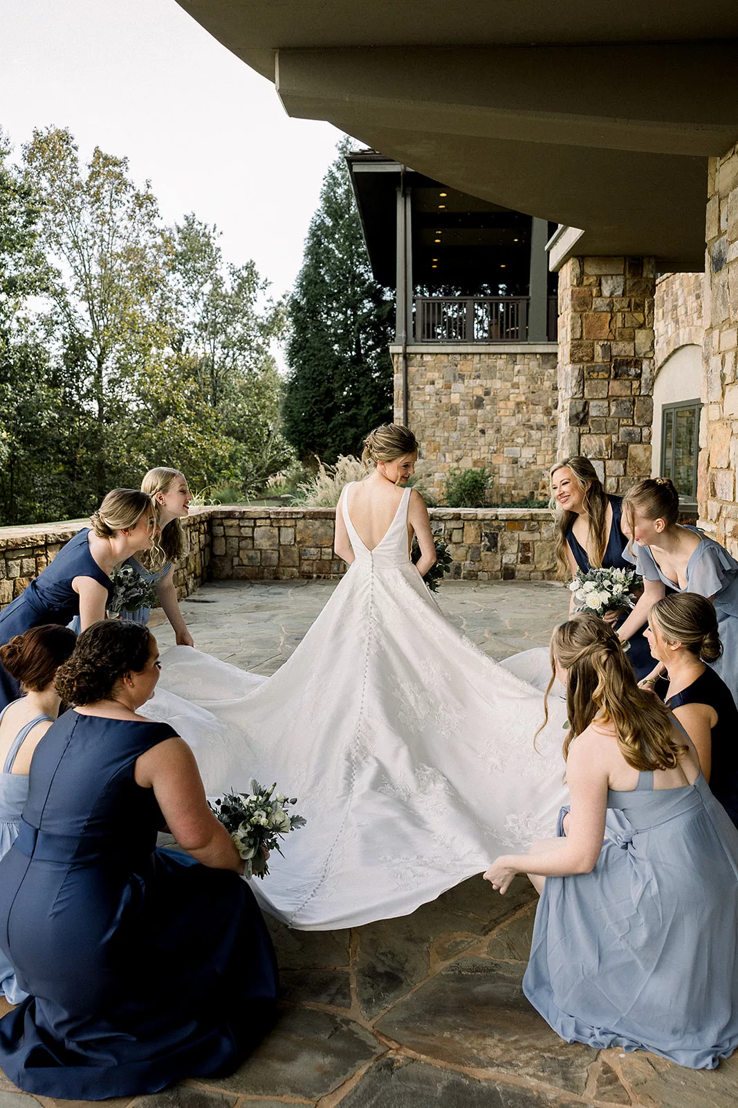 A bride stands while her bridal party spreads out her dress