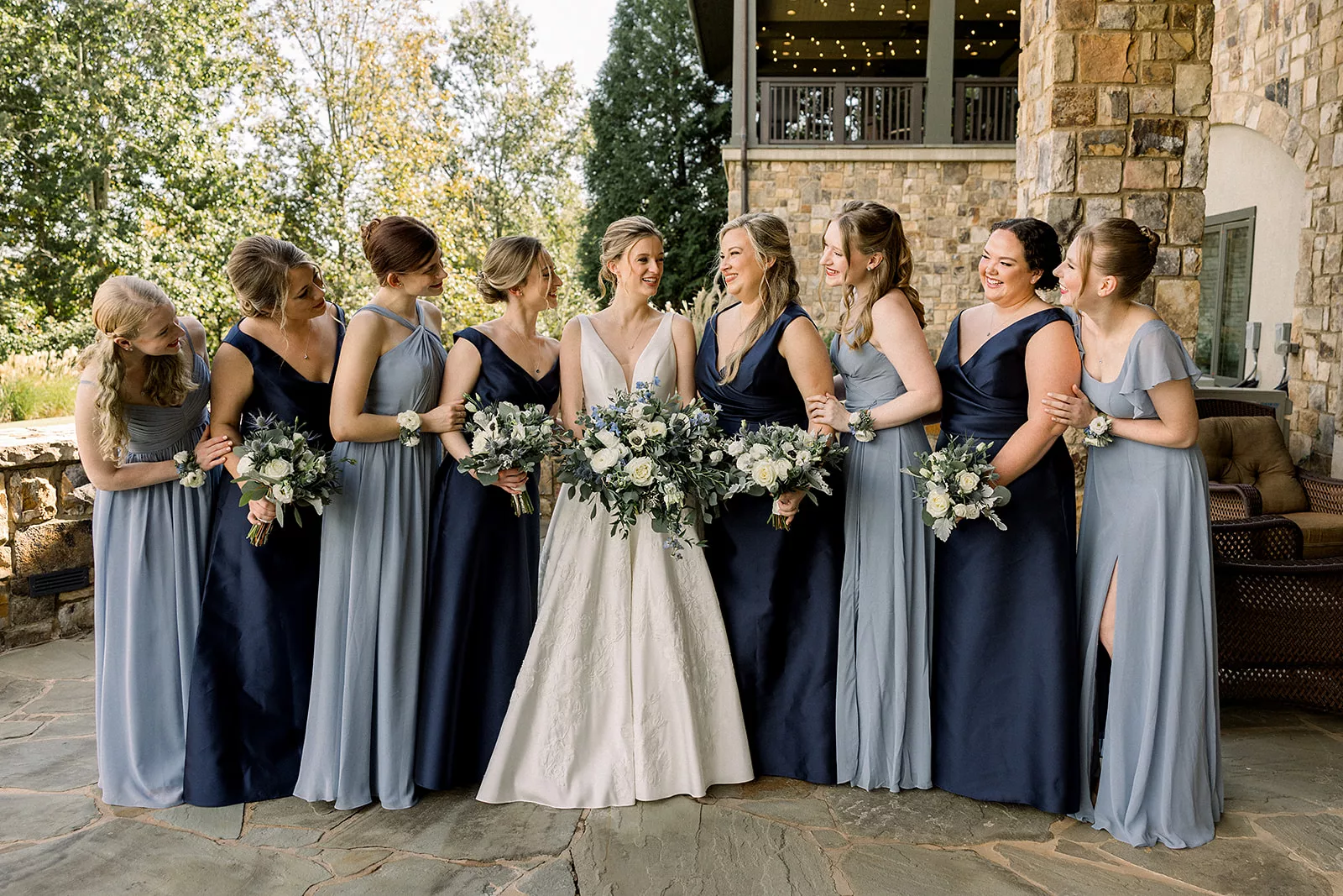 A bride laughs with her bridal party on a stone patio