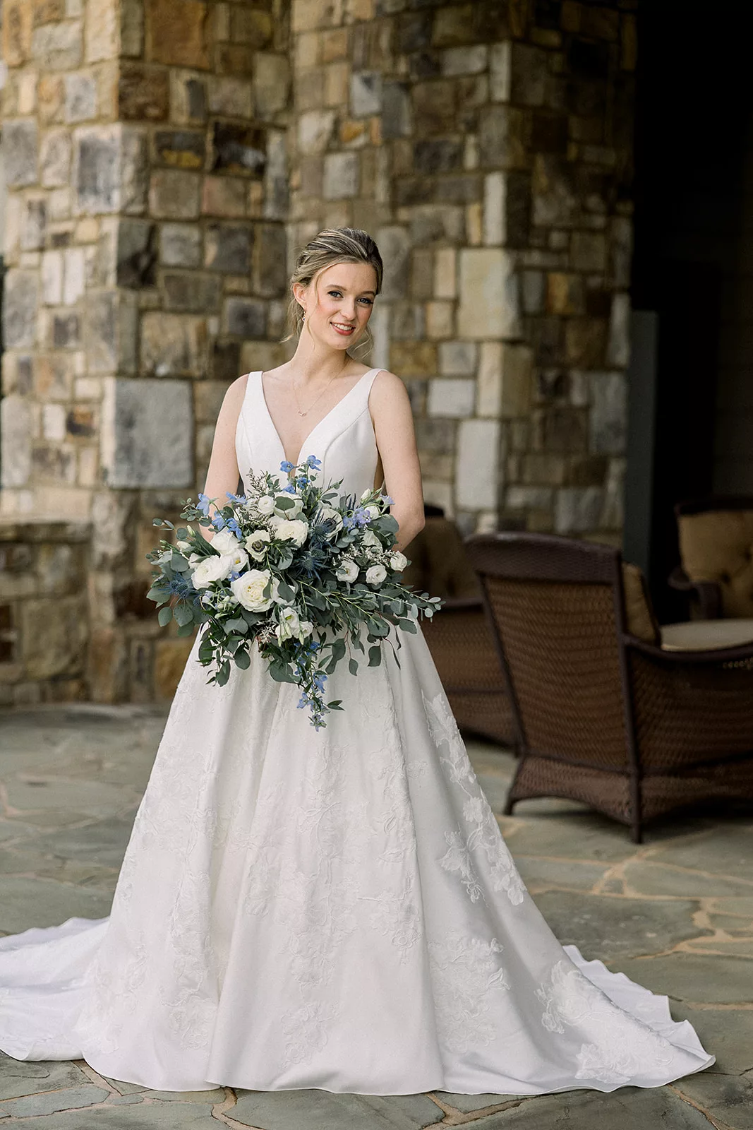 A bride stands on a stone patio holding her flowers