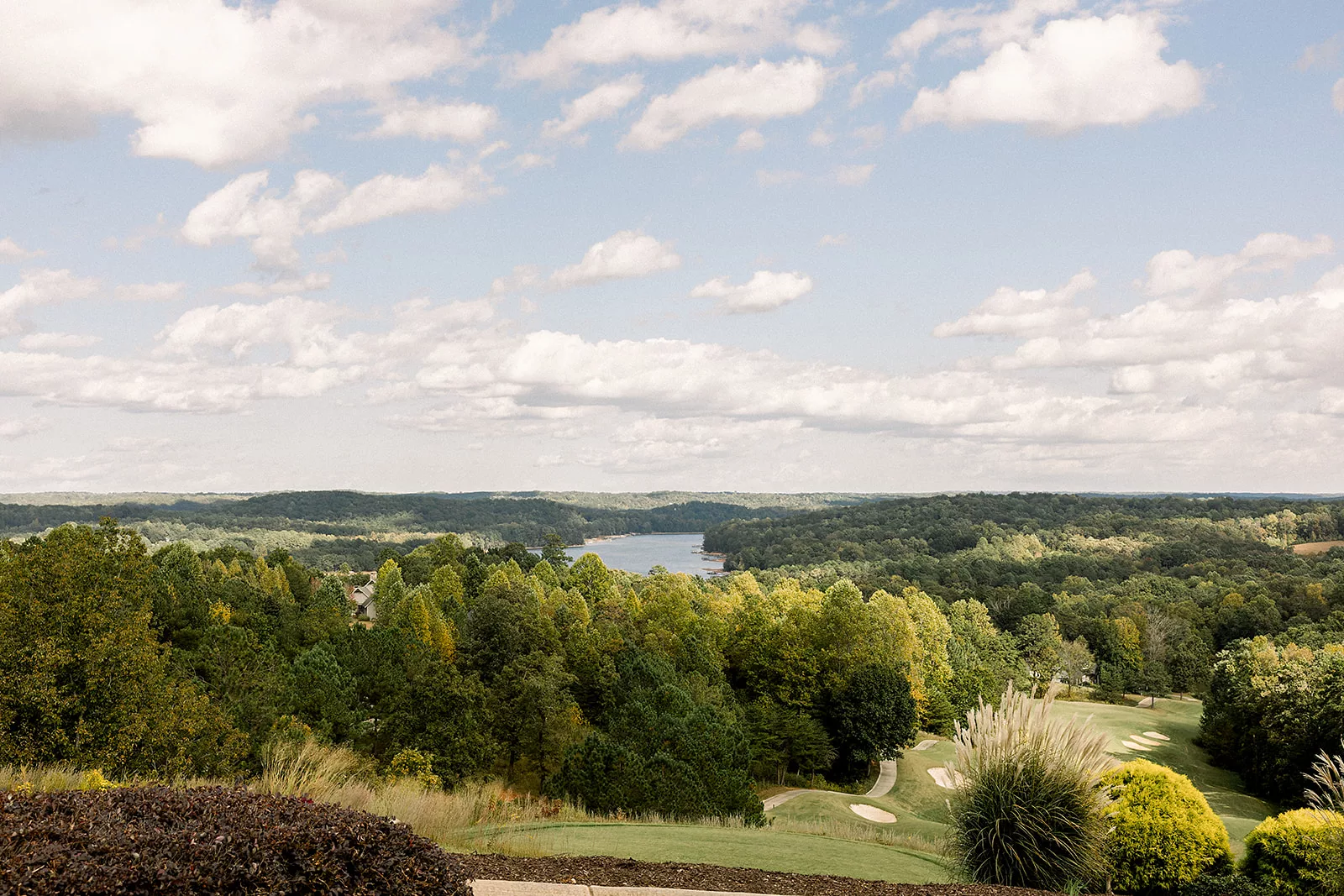 A wide shot of a golf course going downhill and a lake