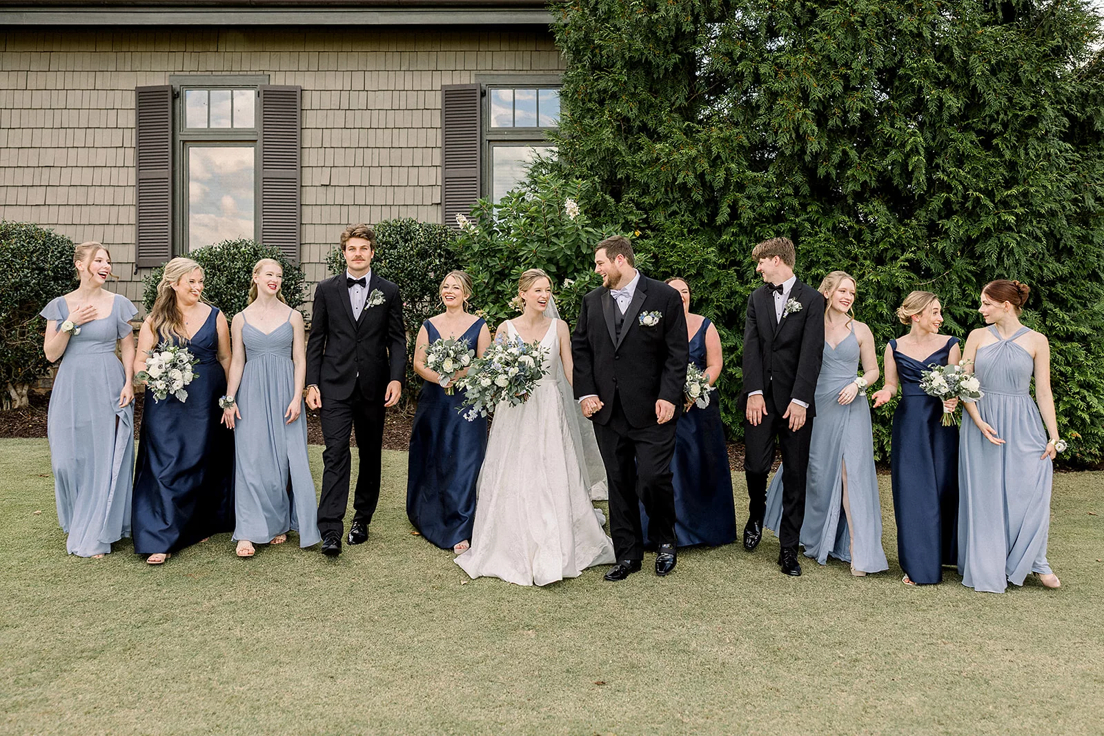 Newlyweds walk through a lawn with their bridal party surrounding them