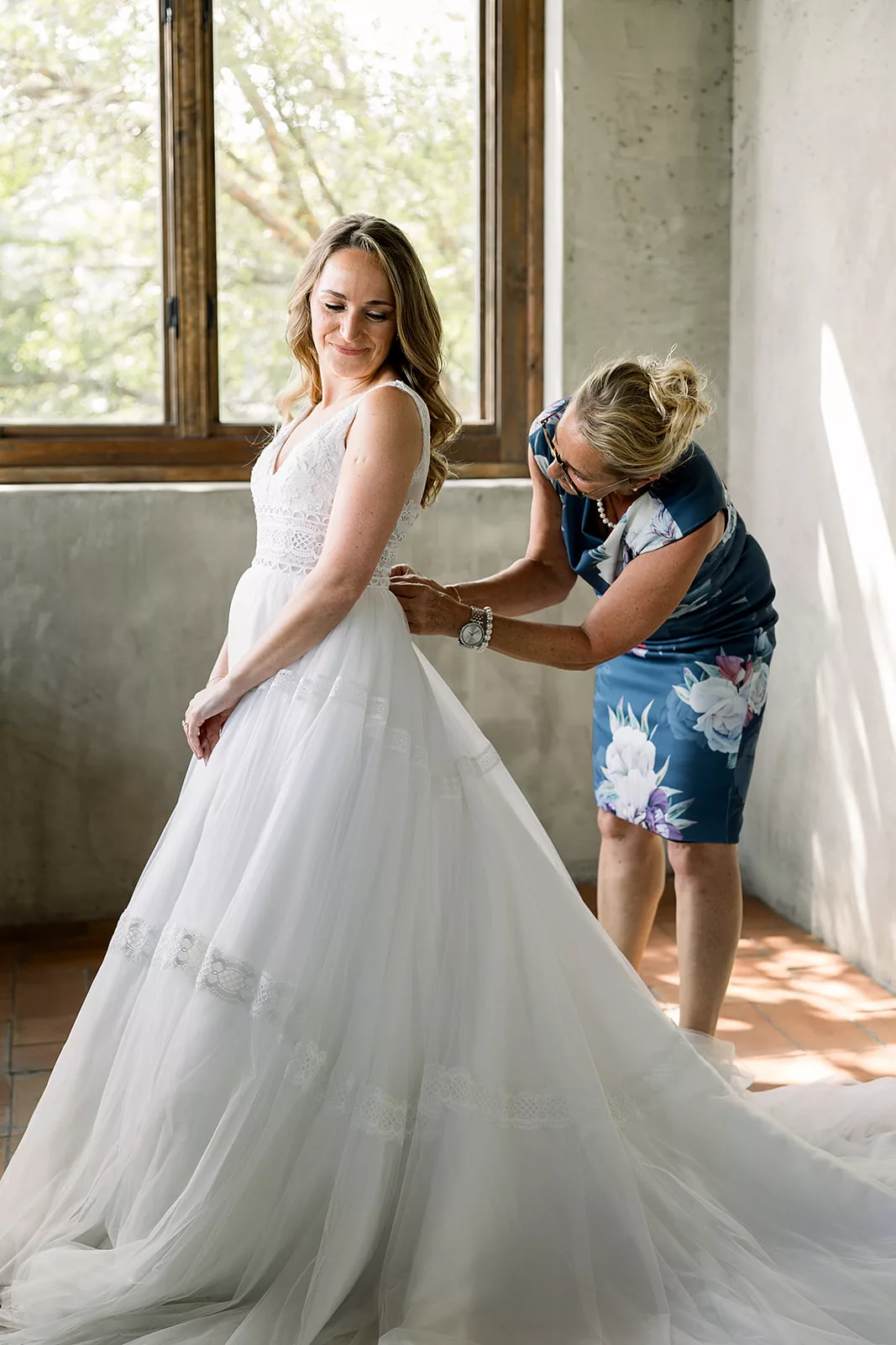 A bride is buttoned into her dress by her mother