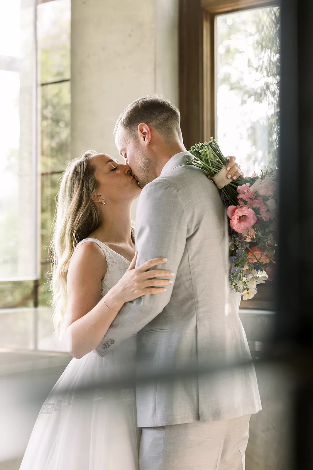 Newlyweds kiss in front of a mirror in a grey suit and lace dress