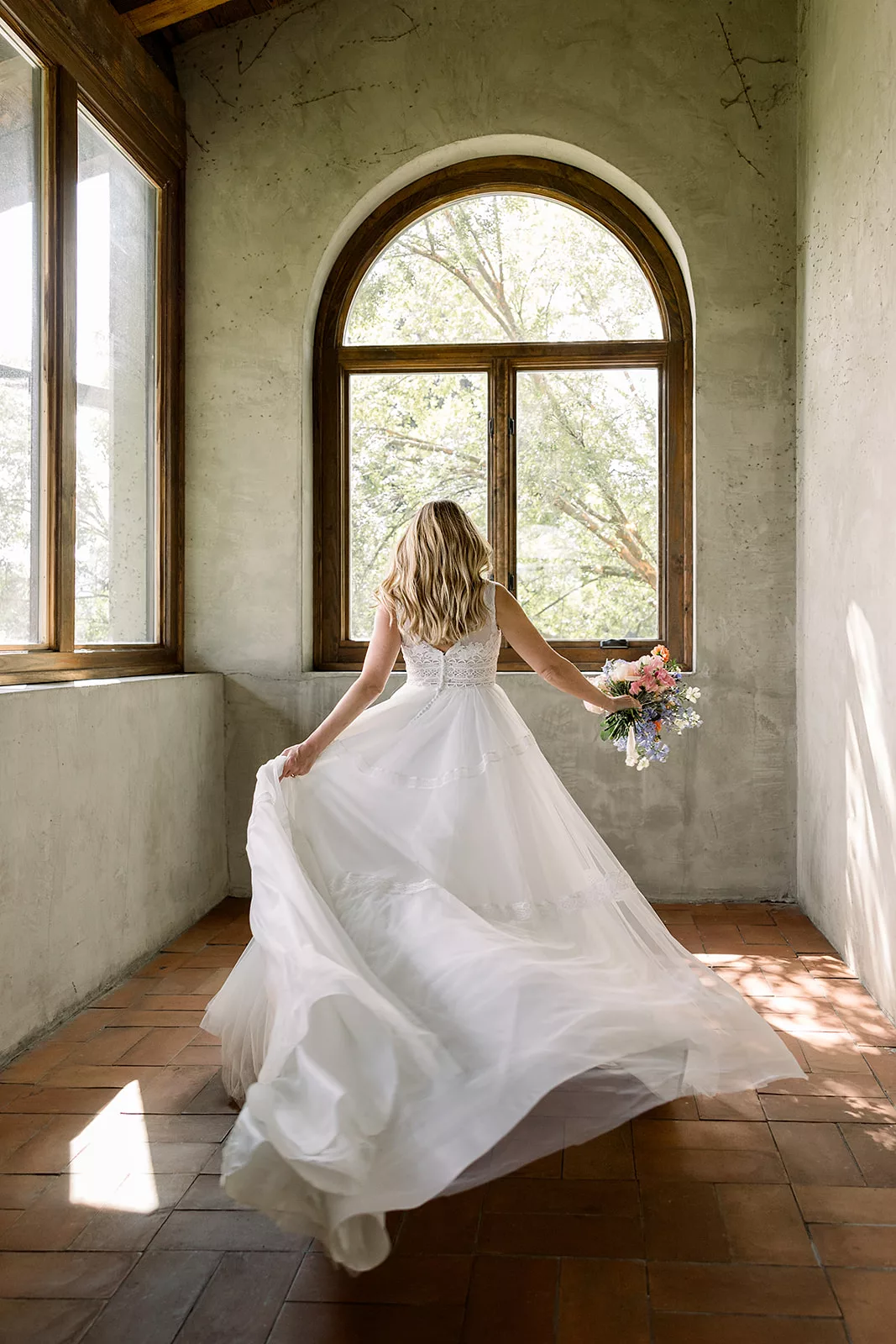 A bride twirls in her dress in a room with tall round windows at the Summerour Studio Wedding venue