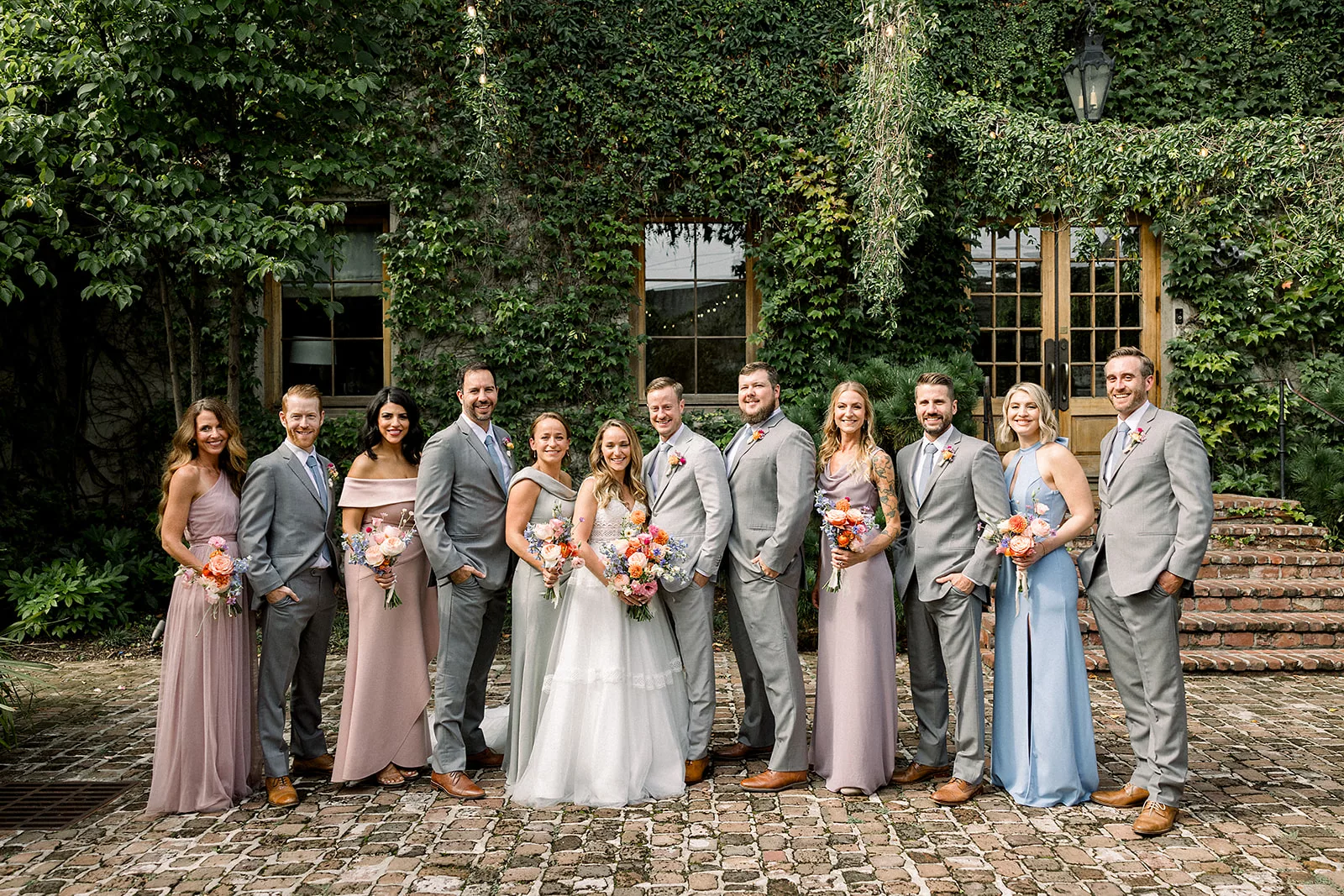 A wedding party stands on either side of newlyweds on a brick patio of an ivy covered building at a Summerour Studio Wedding