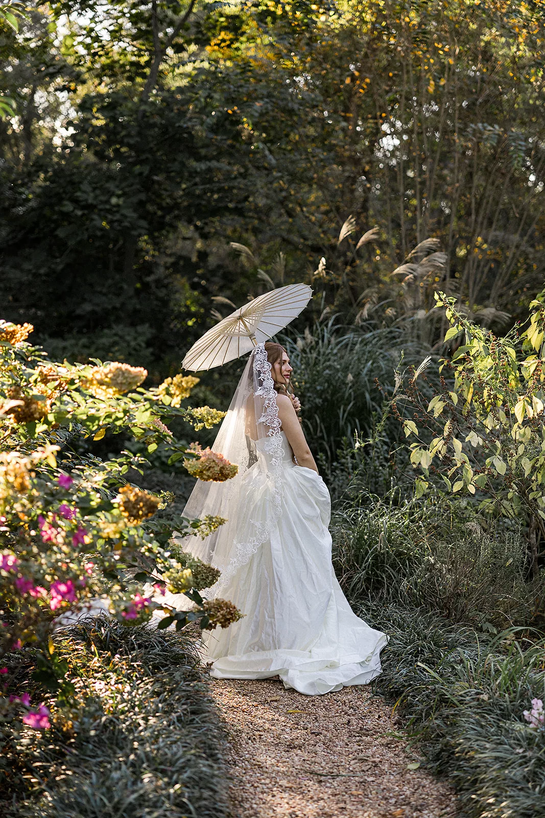 A bride stands in a Wildflower 301 garden path holding an umbrella