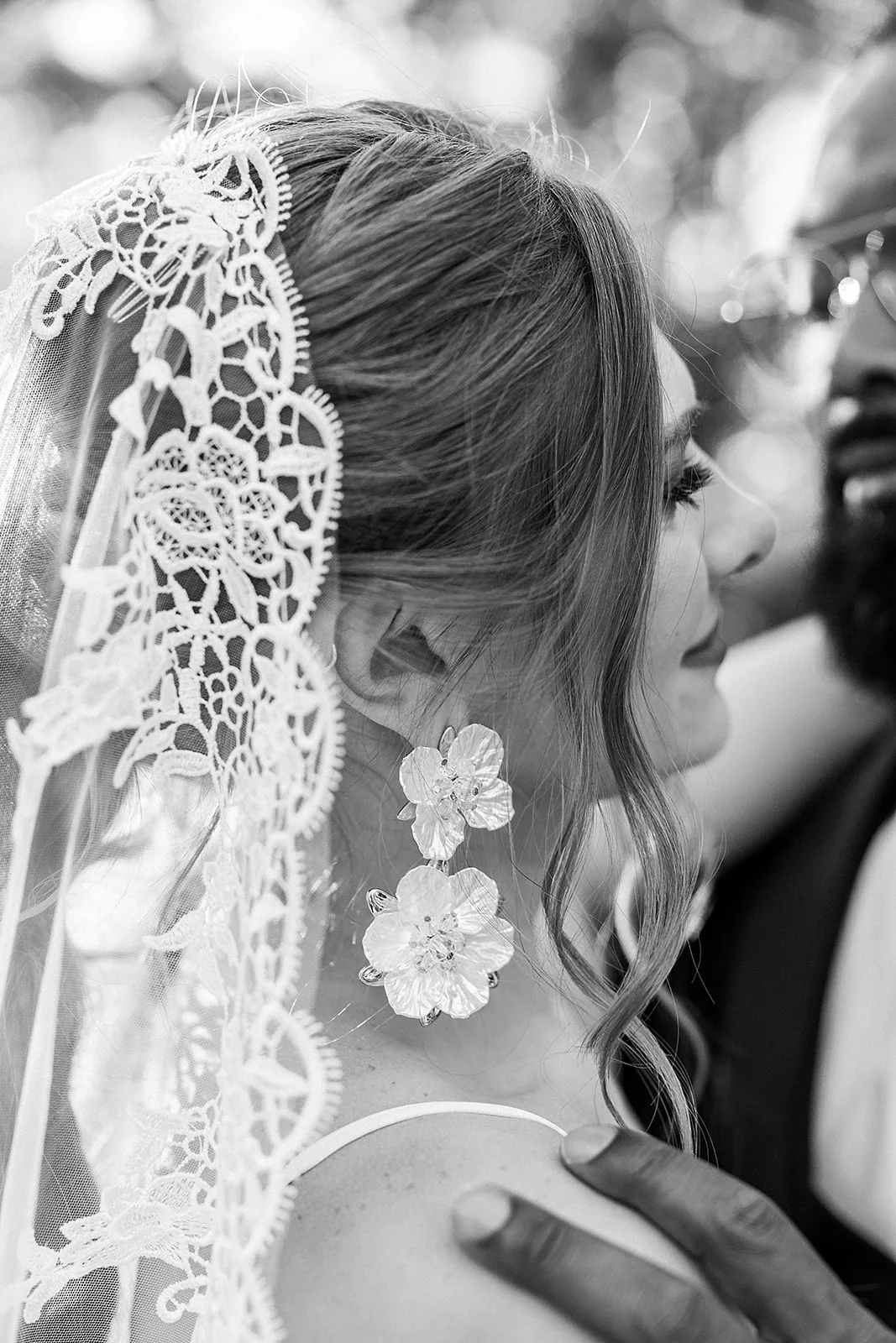 Details of a bride's lace veil as she hugs her groom
