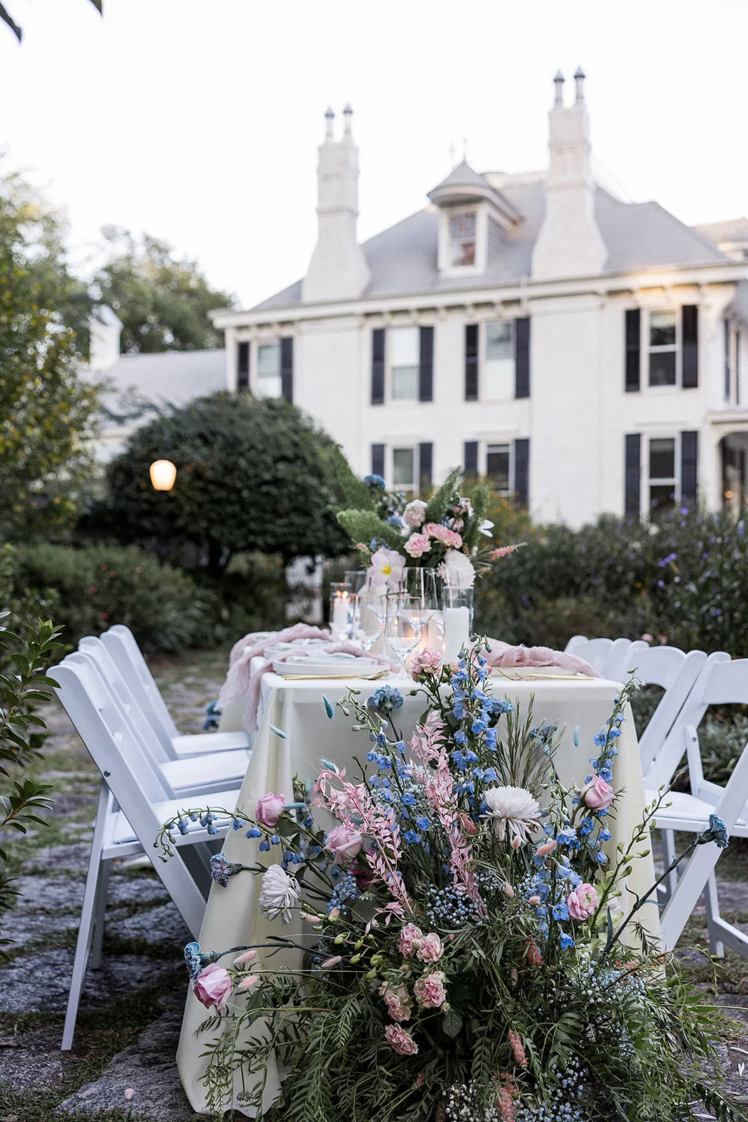 Details of an outdoor Wildflower 301 wedding reception table with blue and pink florals and white chairs in a garden