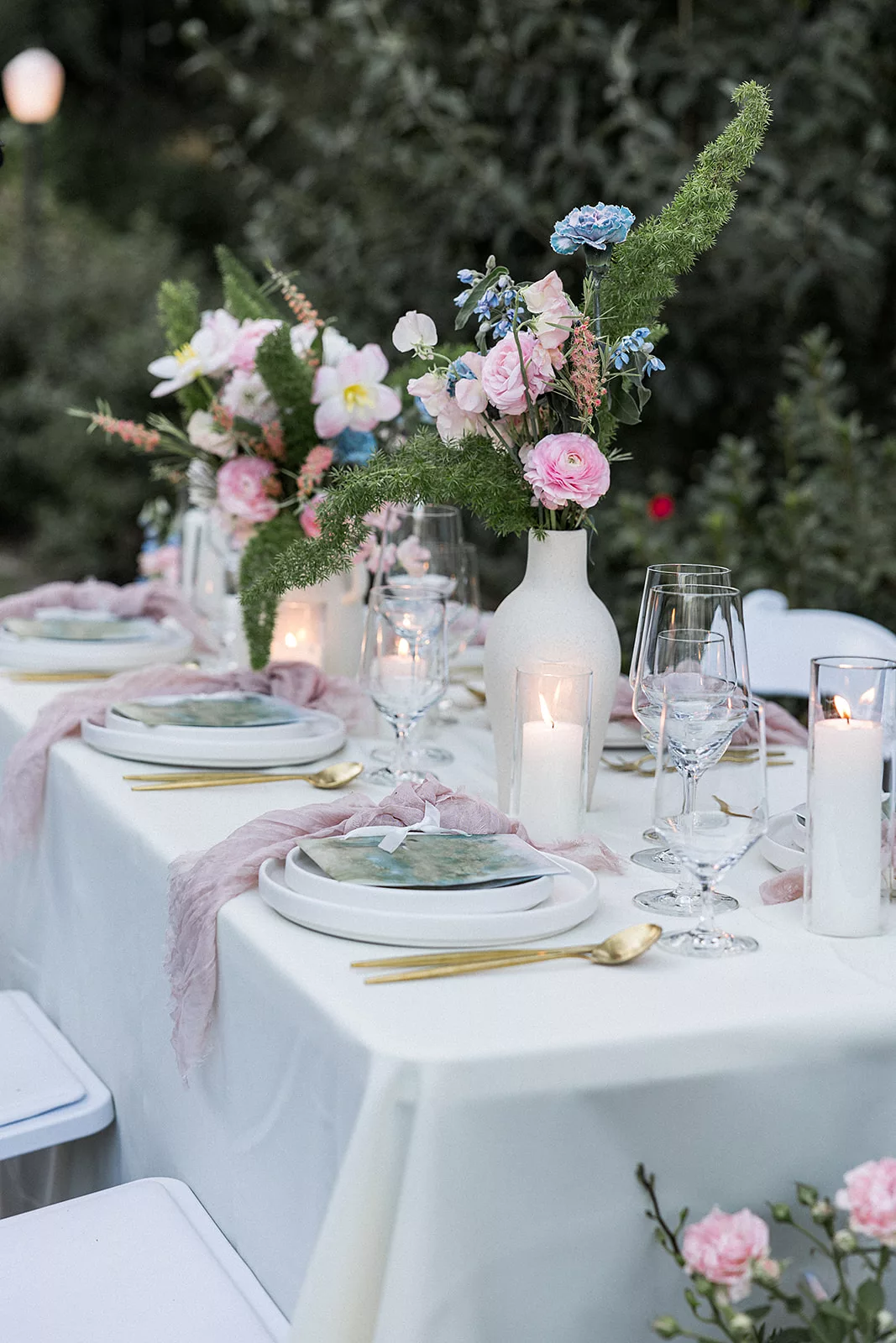 Details of a table setting with pink and blue florals/linens and gold silverware at an outdoor Wildflower 301 wedding reception