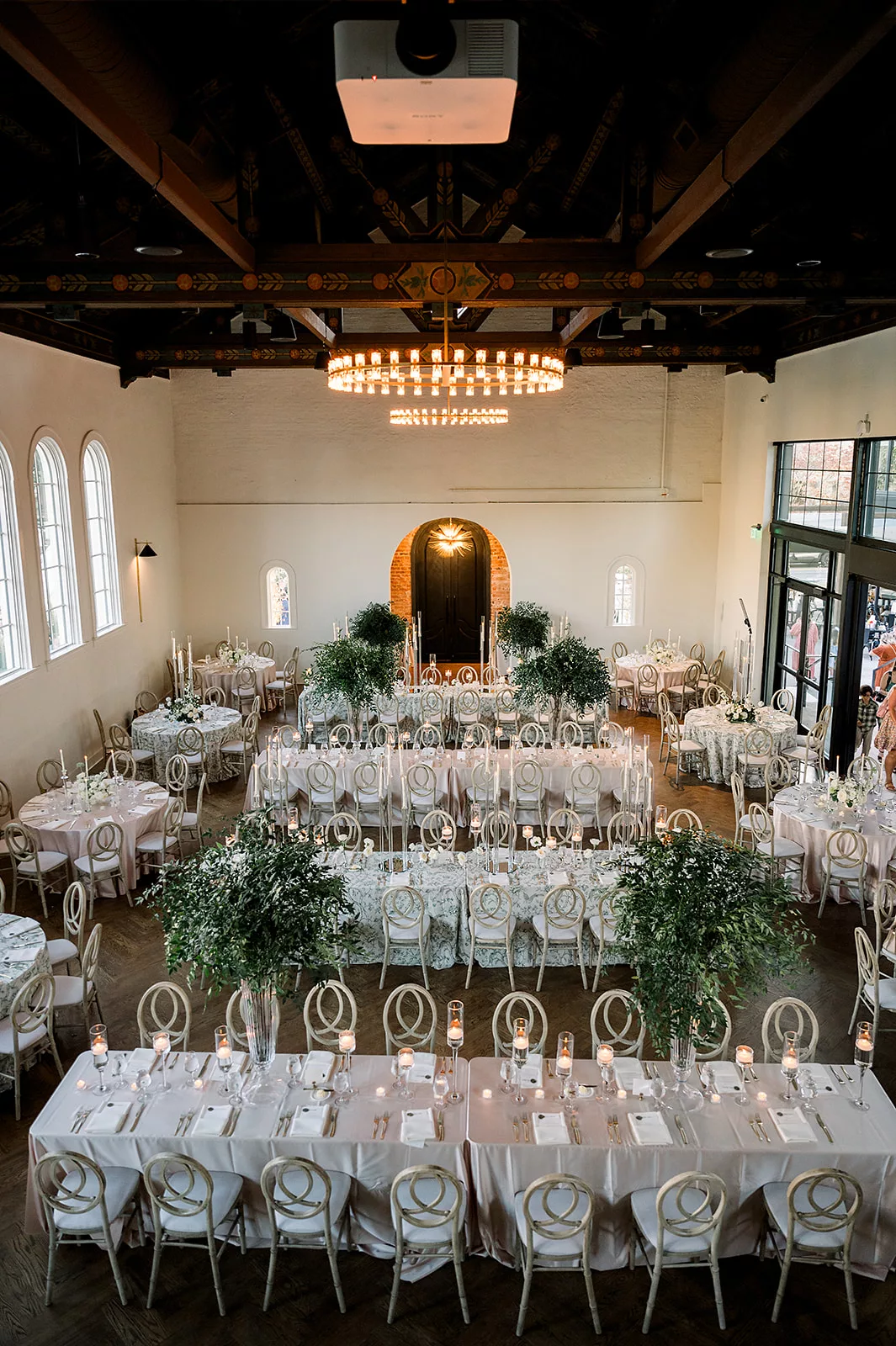 Above look at a wedding reception set up indoors with tall centerpieces and floral linens