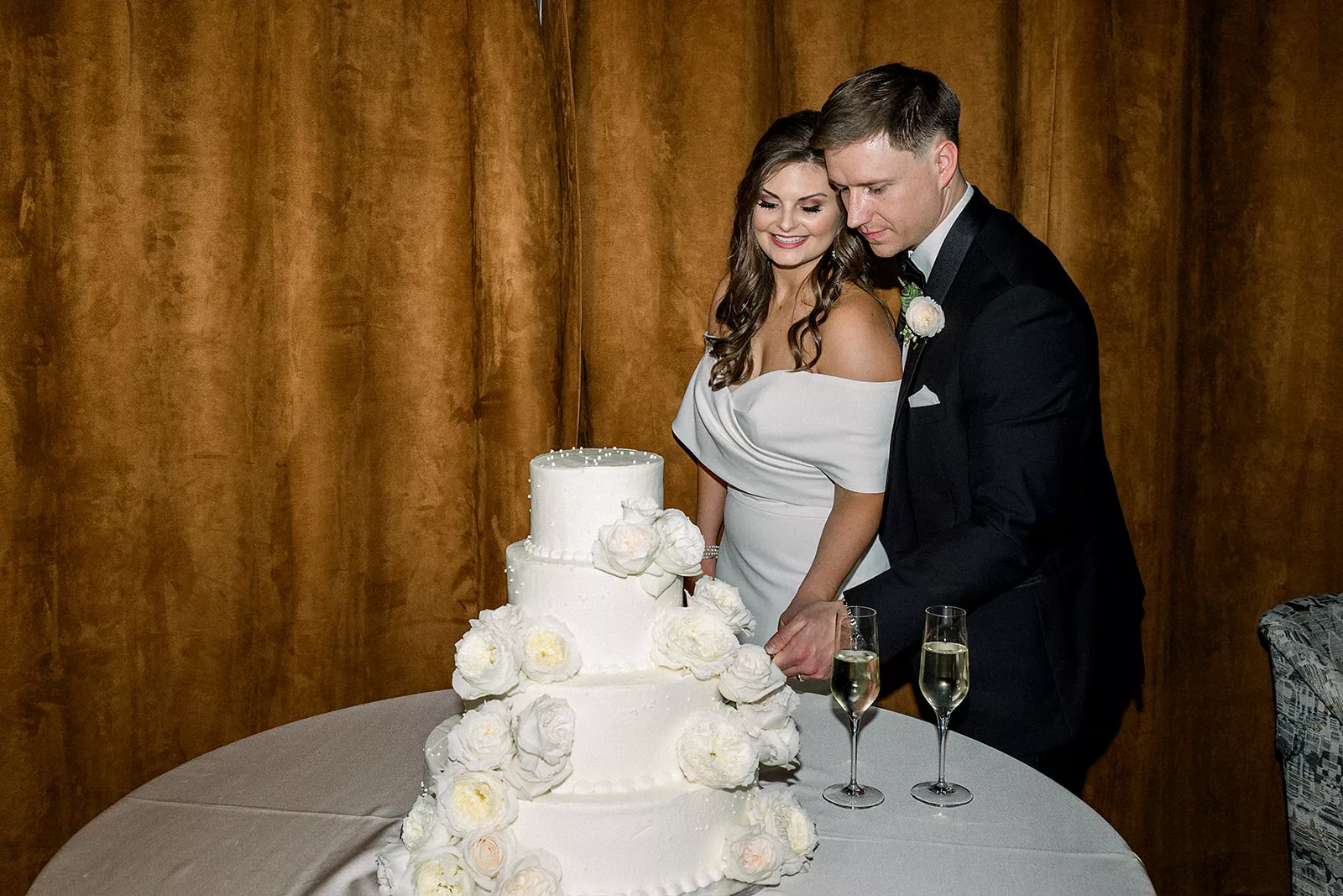 Newlyweds cut their four tier white cake with white roses on it