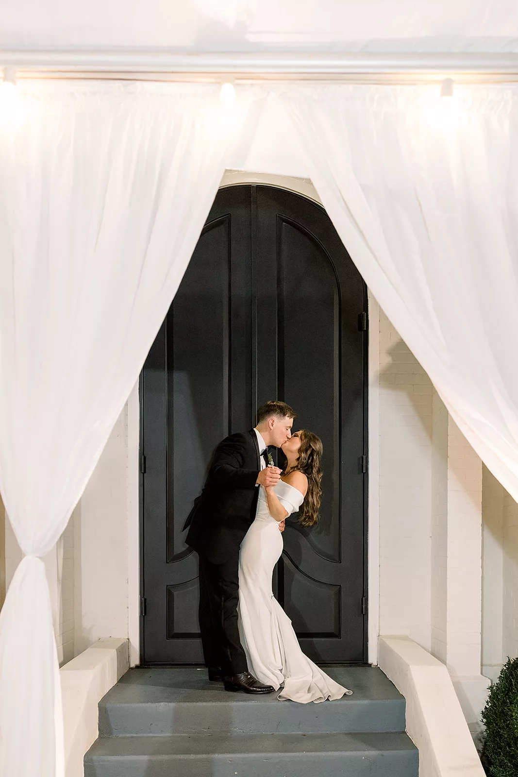 Newlyweds kiss at the large front doors of the The Chapel Athens wedding venue