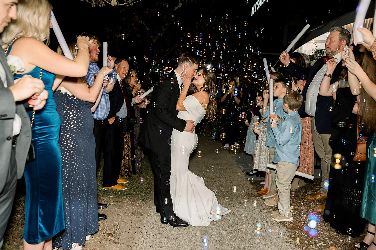 Newlyweds kiss under a shower of bubbles while exiting their The Chapel Athens wedding