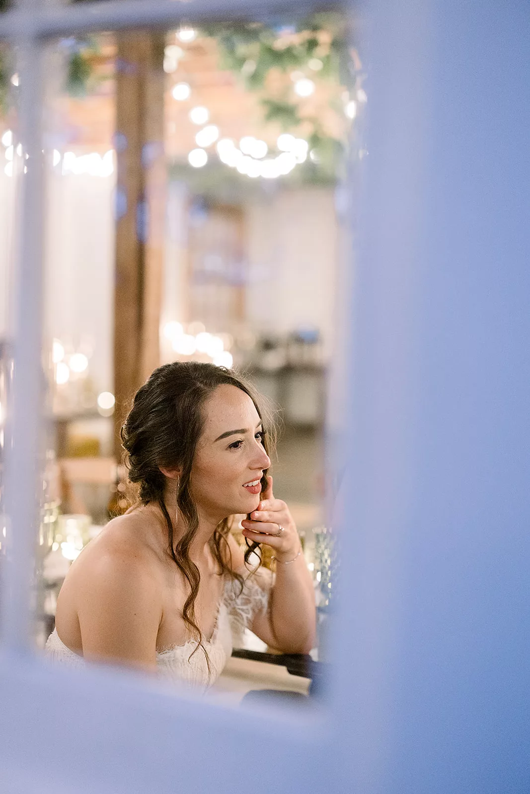 A bride sits inside a window at a reception table