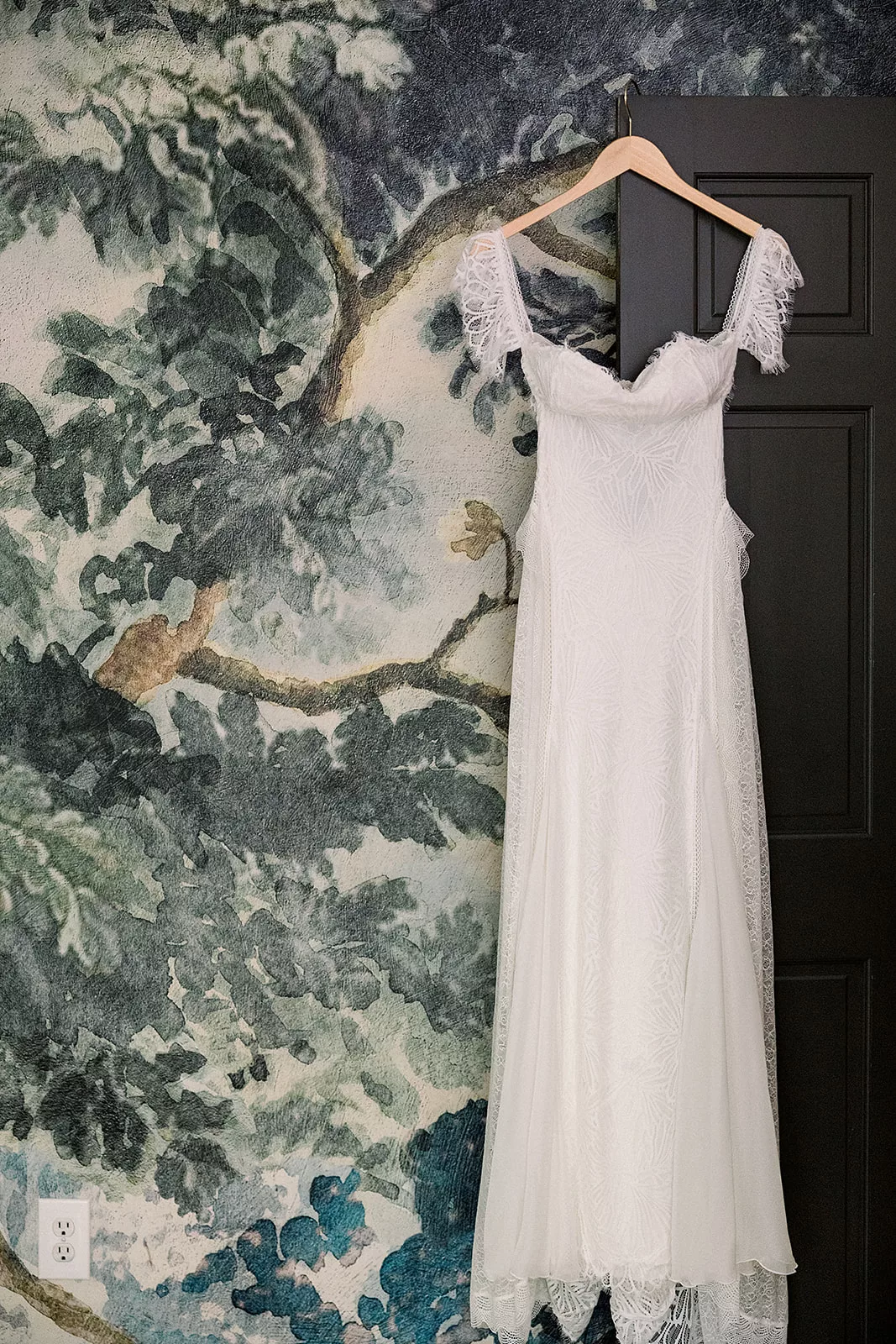 A wedding dress hangs from a door against a forest mural