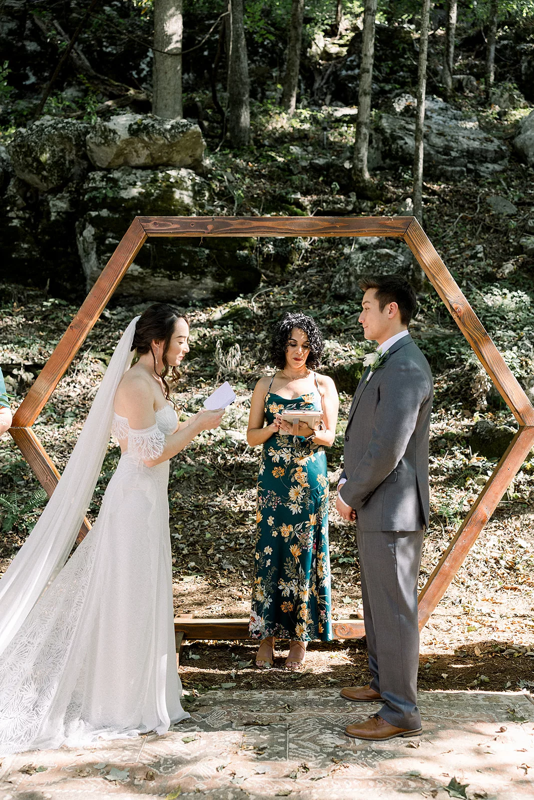 Newlyweds read each other their vows in front of a wooden beam arbor in the forest