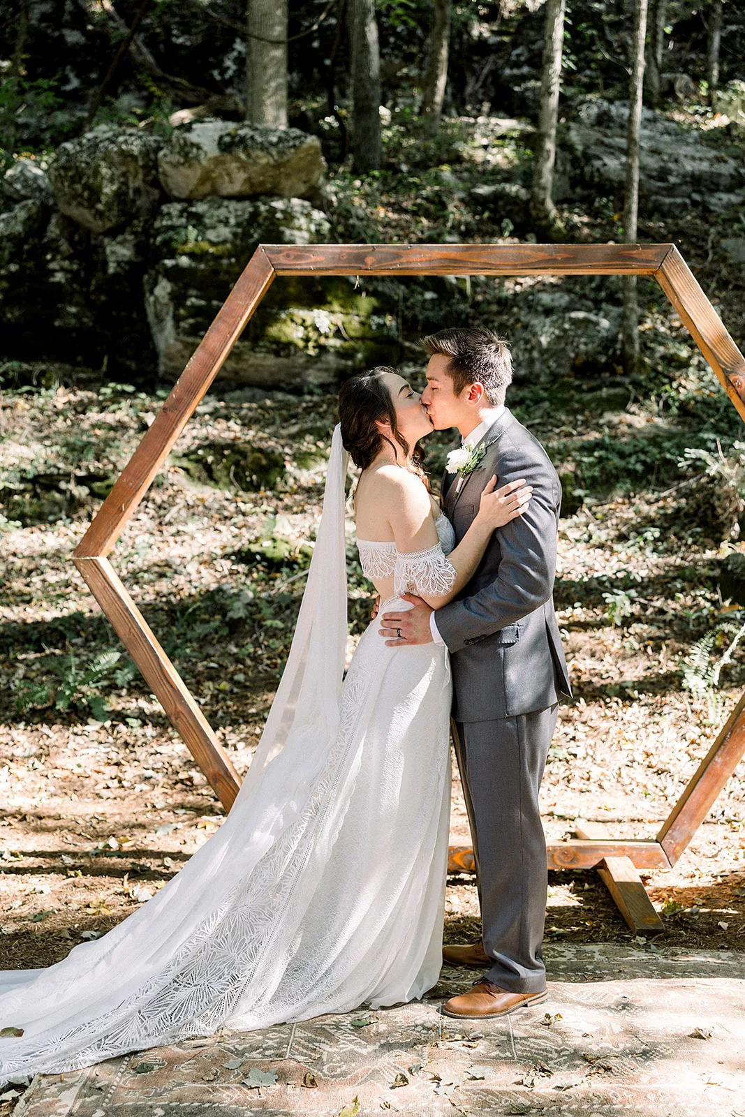 Newlyweds kiss under a wooden beam arbor in the woods to finish their Sustainable Wedding Venue ceremony