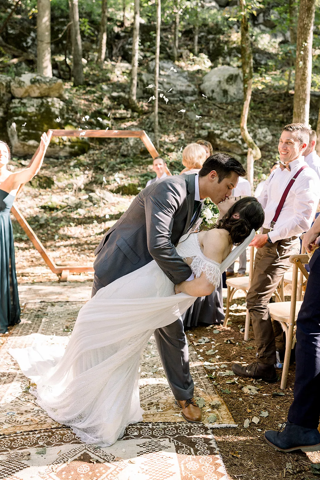 A groom dips and kisses his bride to finish their wedding ceremony with guests celebrating around them