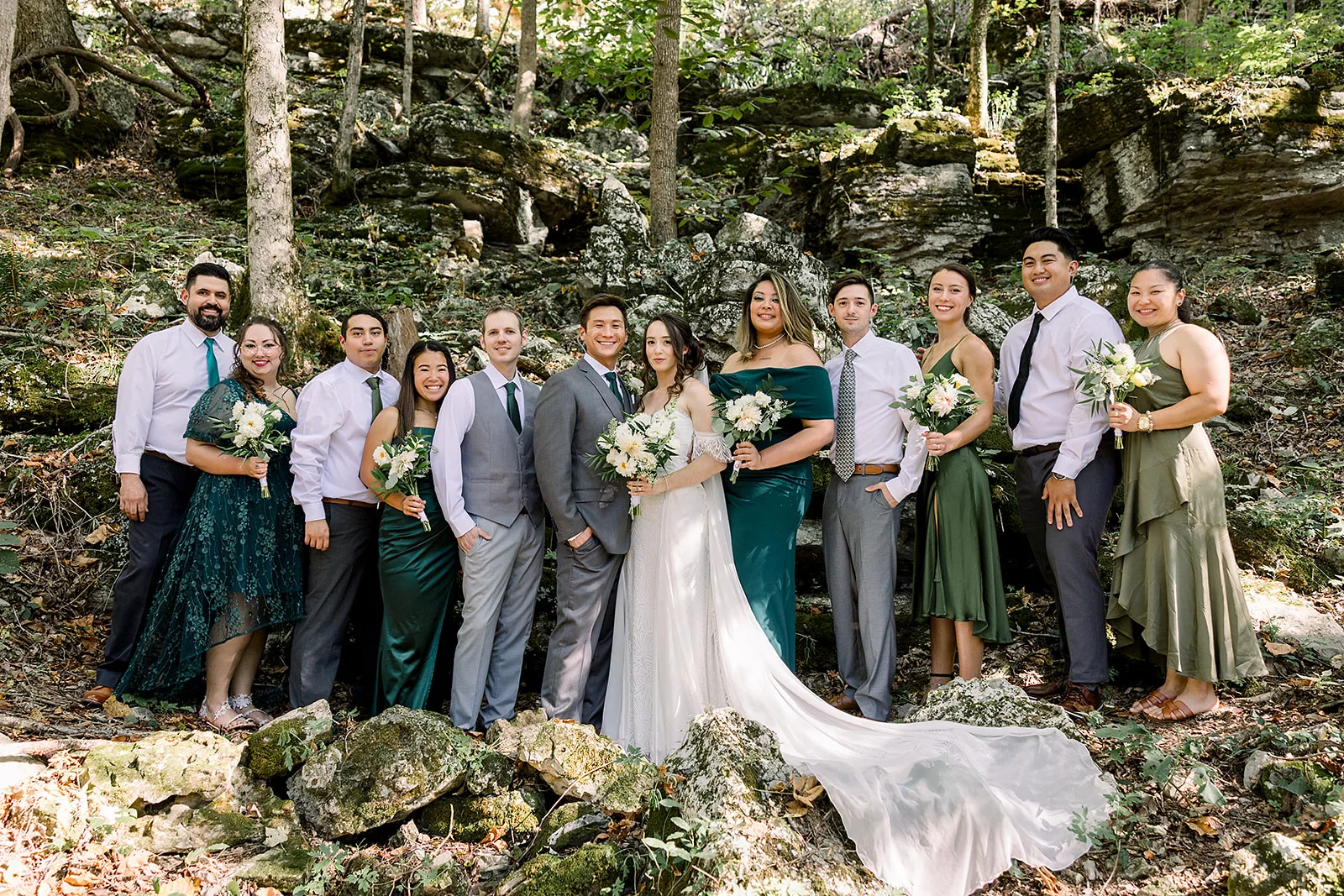 Newlyweds stand with their wedding party on a mountain trail in the forest