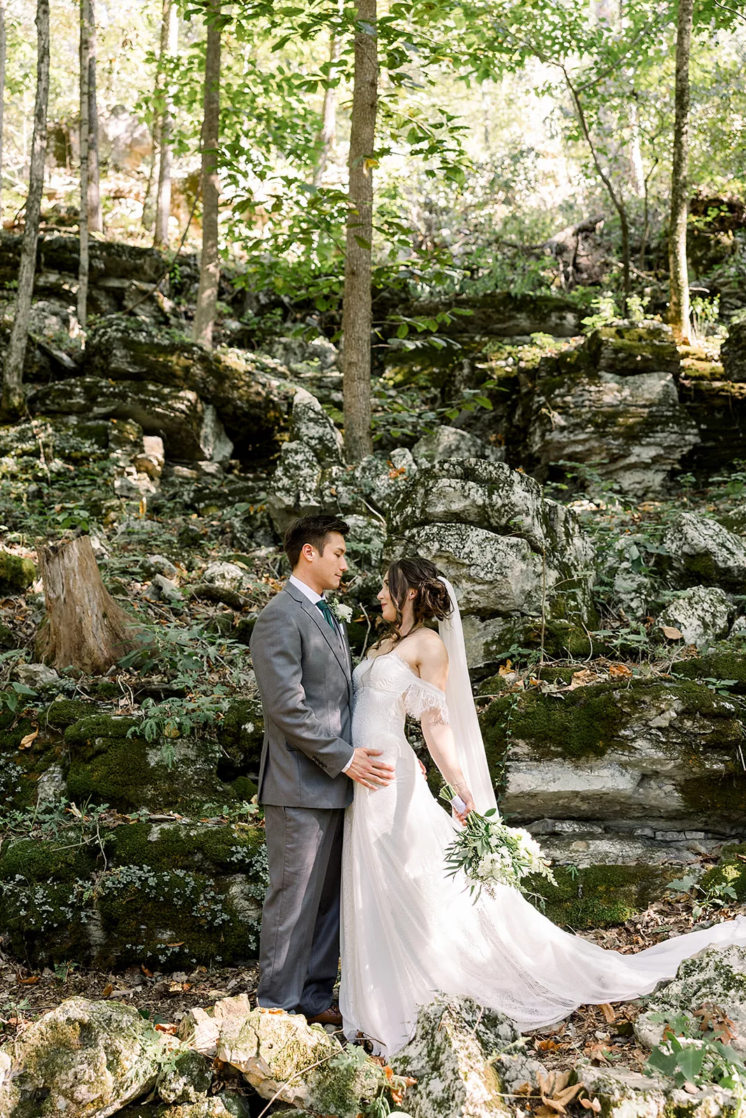 Newlyweds stand together on the edge of a rocky hill in the forest at their Sustainable Wedding Venue